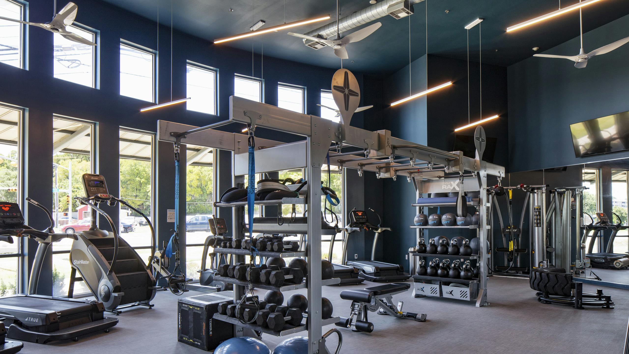 24 hour fitness zone at AMLI South Shore apartments with blue walls featuring cardio and weigh training machines and dumbbells