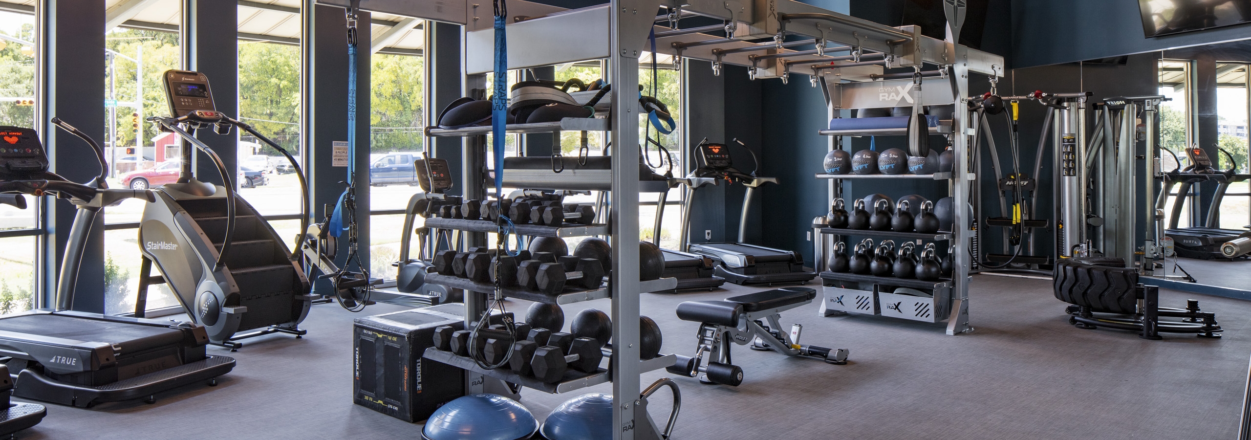 24 hour fitness zone at AMLI South Shore apartments with blue walls featuring cardio and weigh training machines and dumbbells