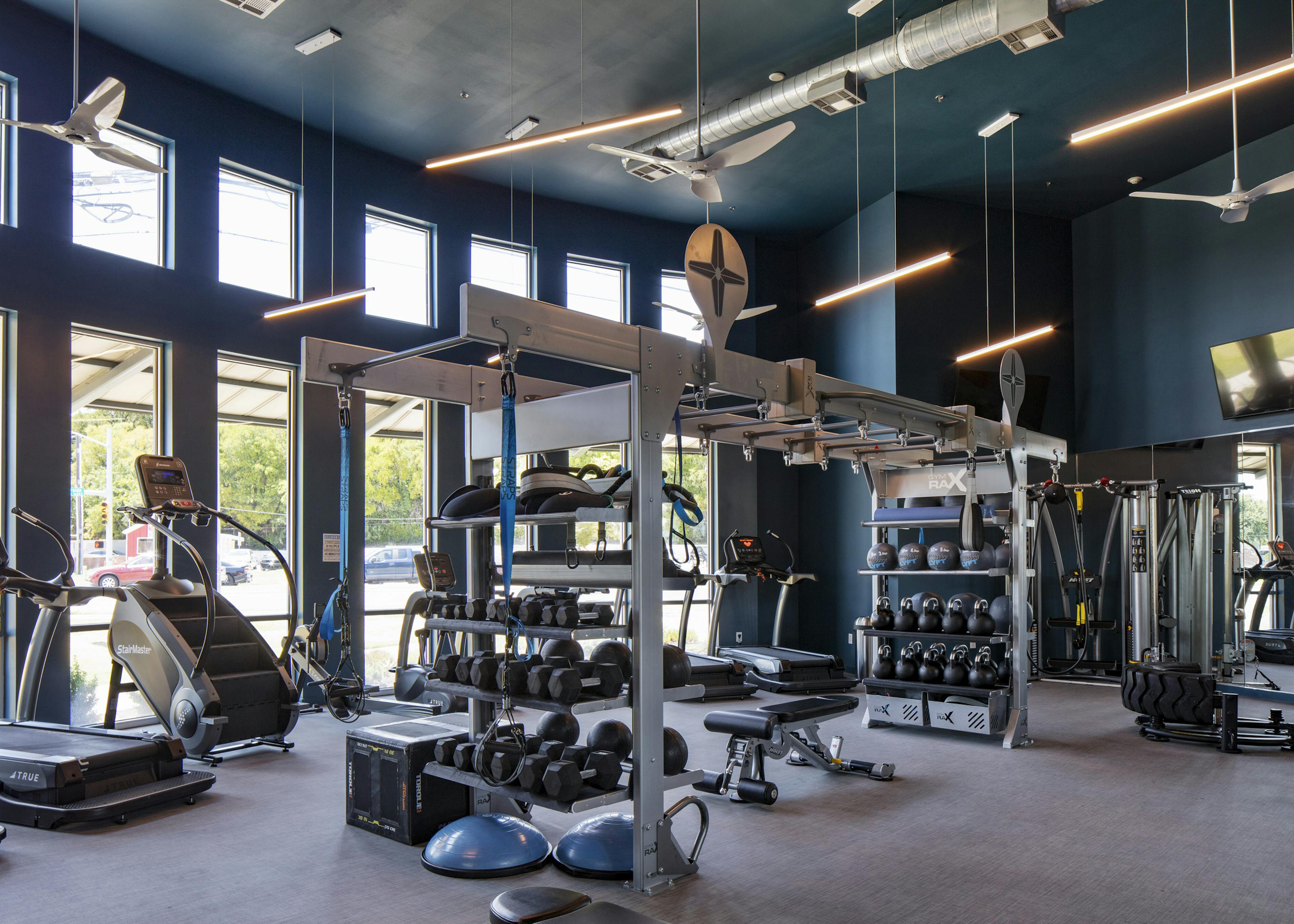 24 hour fitness zone at AMLI South Shore apartments with blue walls featuring cardio and weigh training machines and dumbbells