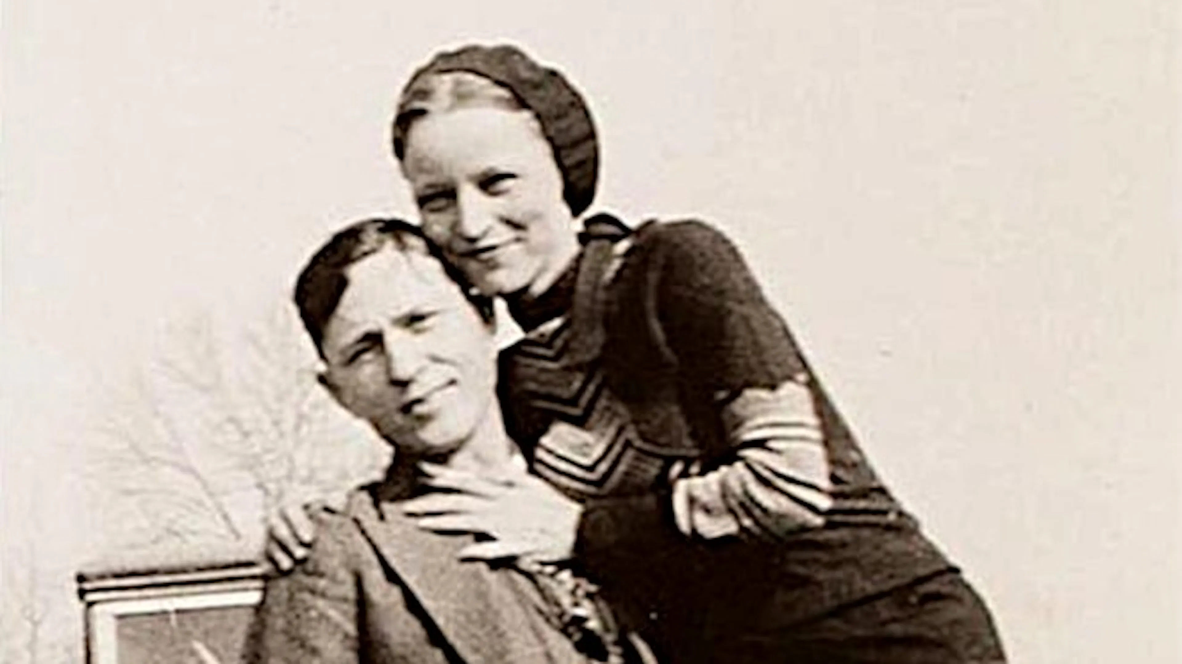 Clyde Barrow and Bonnie Parker smiling for a photo in front of their car