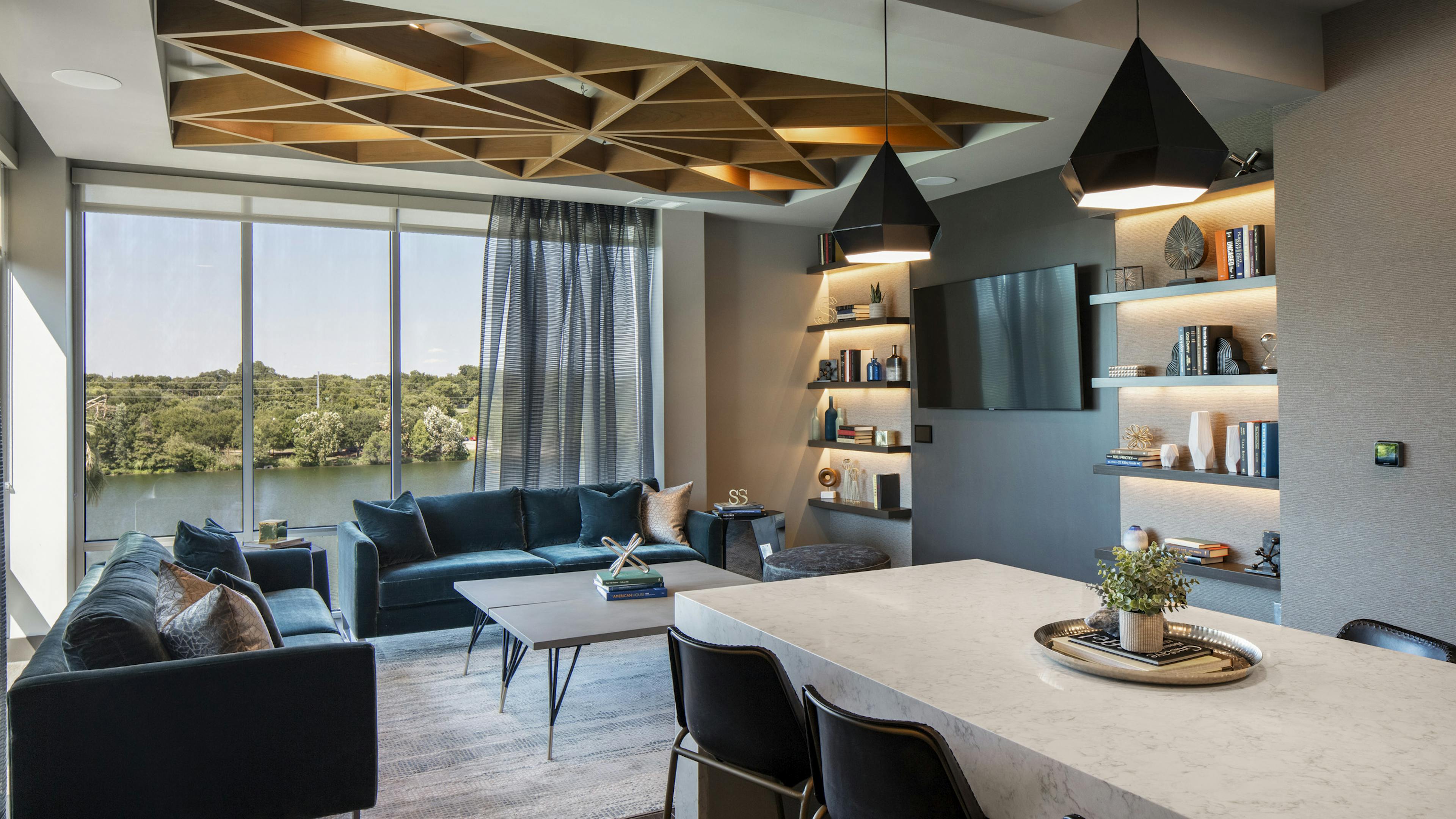 Resident lounge at AMLI South Shore with blue velvet couches facing a big TV and floor to ceiling windows showcasing the lake