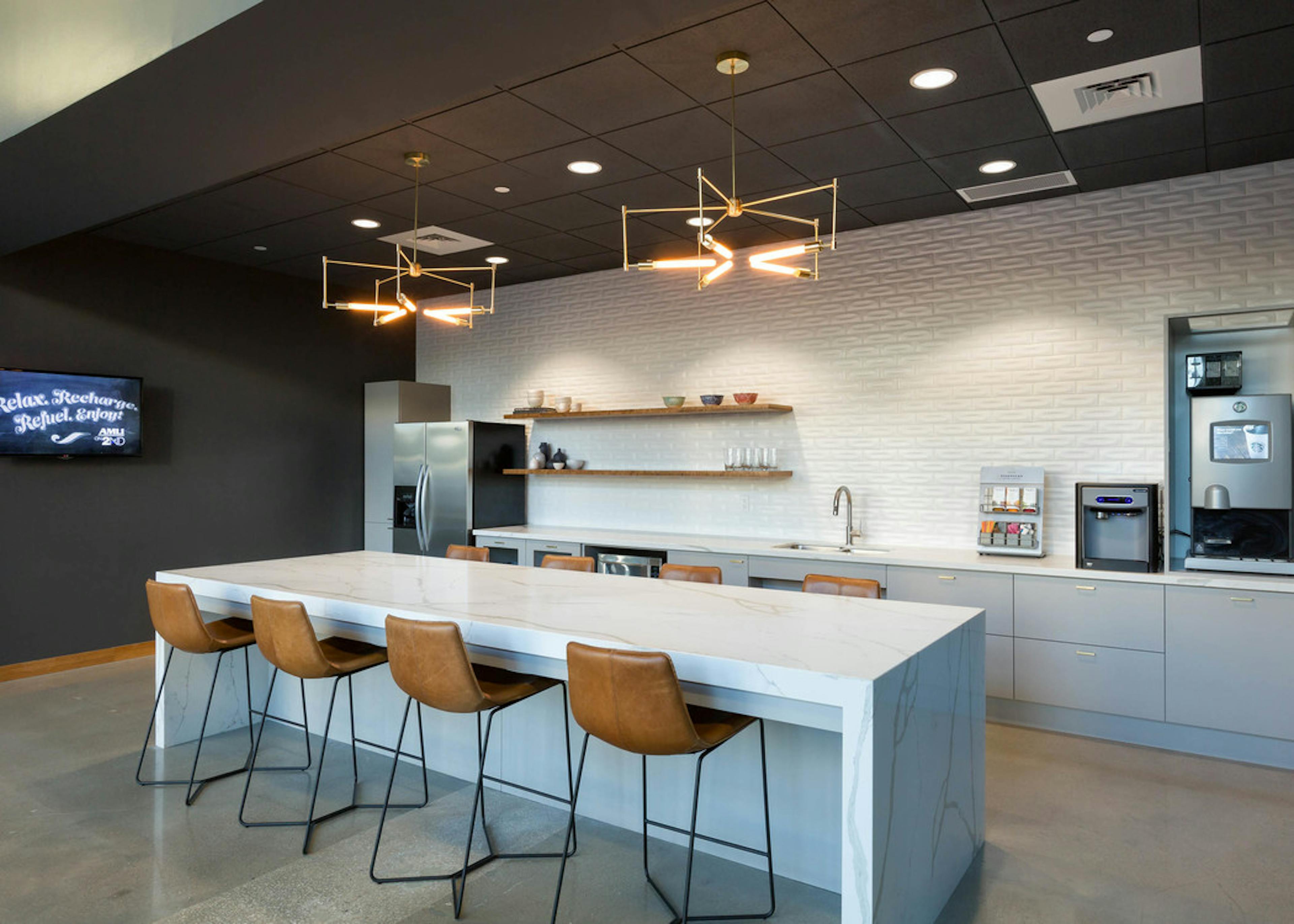 AMLI on 2nd java cafe with grey cabinets and white counters with coffee maker and island with four brown leather barstools 