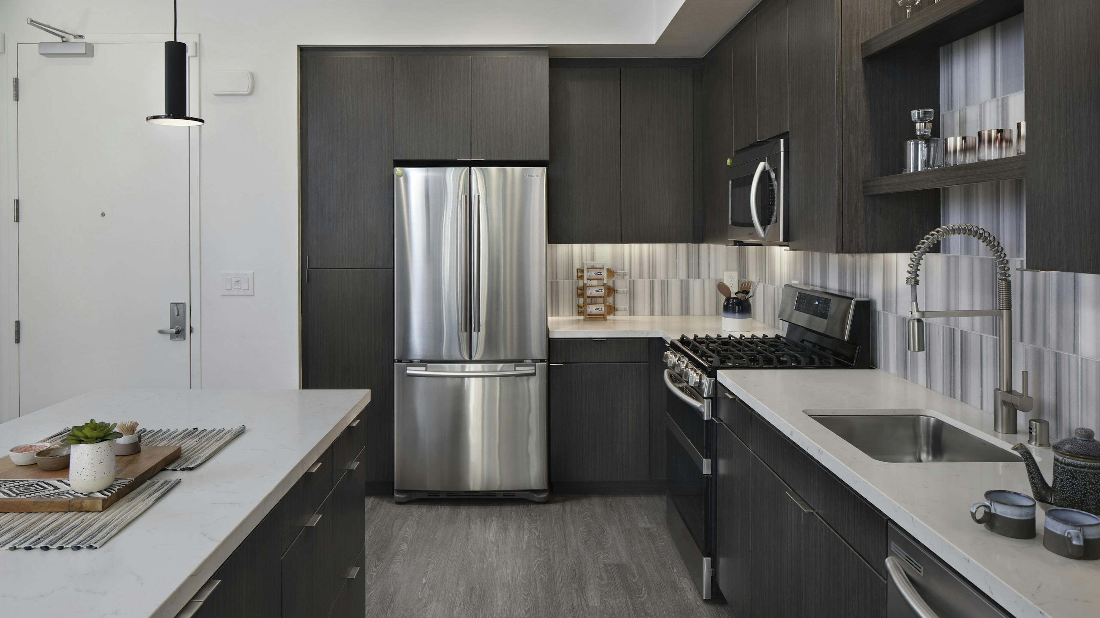 Interior of AMLI Park Broadway kitchen with gray wood floors and stainless steel appliances and designer tile backsplash