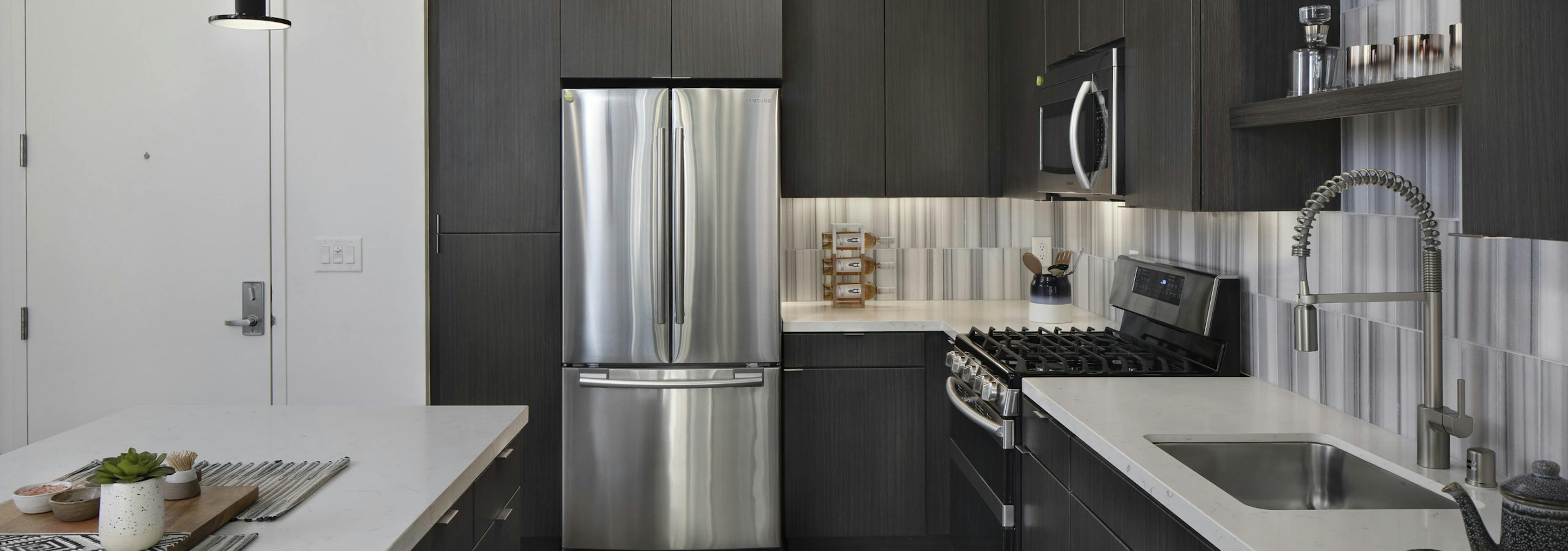Interior of AMLI Park Broadway kitchen with gray wood floors and stainless steel appliances and designer tile backsplash