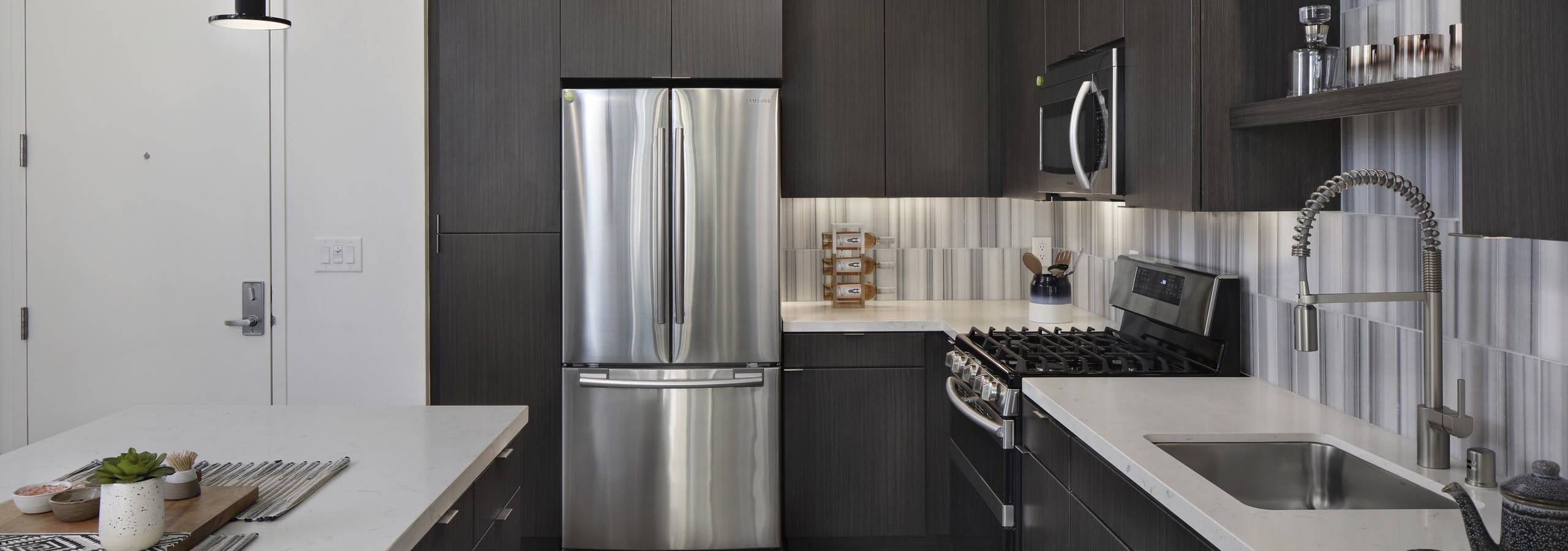 Interior of AMLI Park Broadway kitchen with gray wood floors and stainless steel appliances and designer tile backsplash