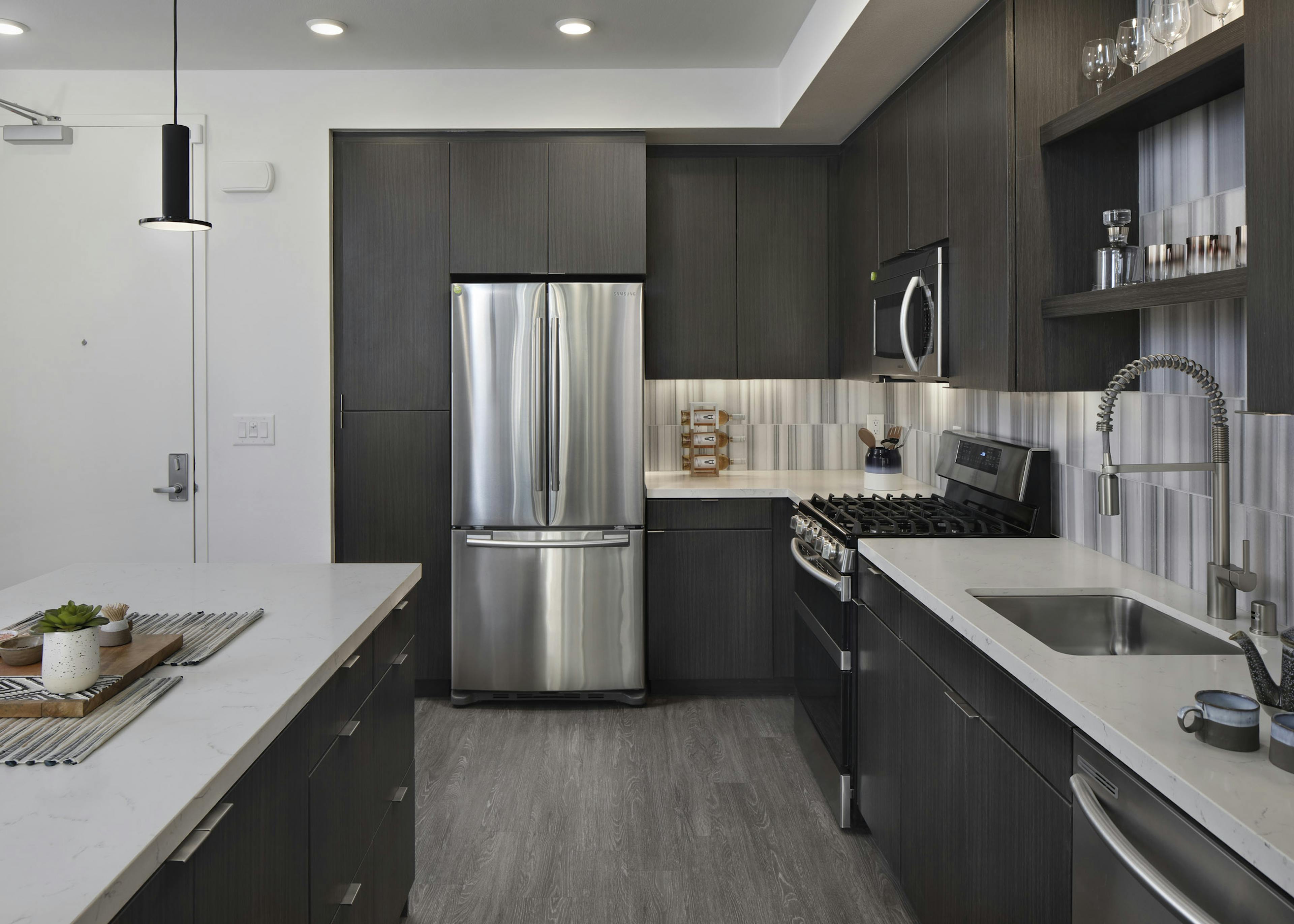Interior of AMLI Park Broadway kitchen with gray wood floors and stainless steel appliances and designer tile backsplash