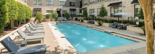 Second courtyard pool at AMLI Las Colinas apartments with surrounding gray lounge chairs and umbrellas and green shrubs