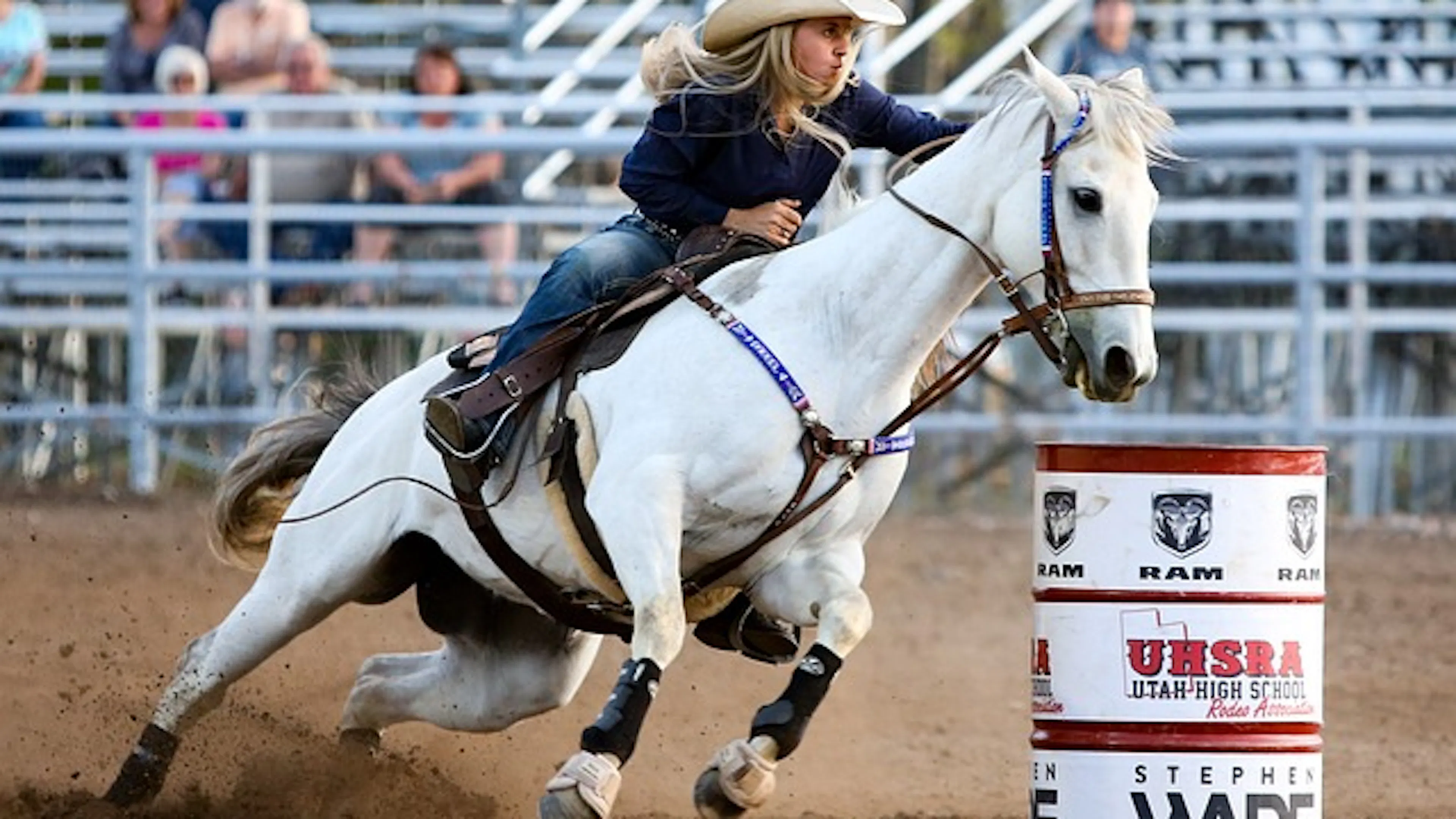 A woman riding a white horse fast around a barrel in a rodeo arena