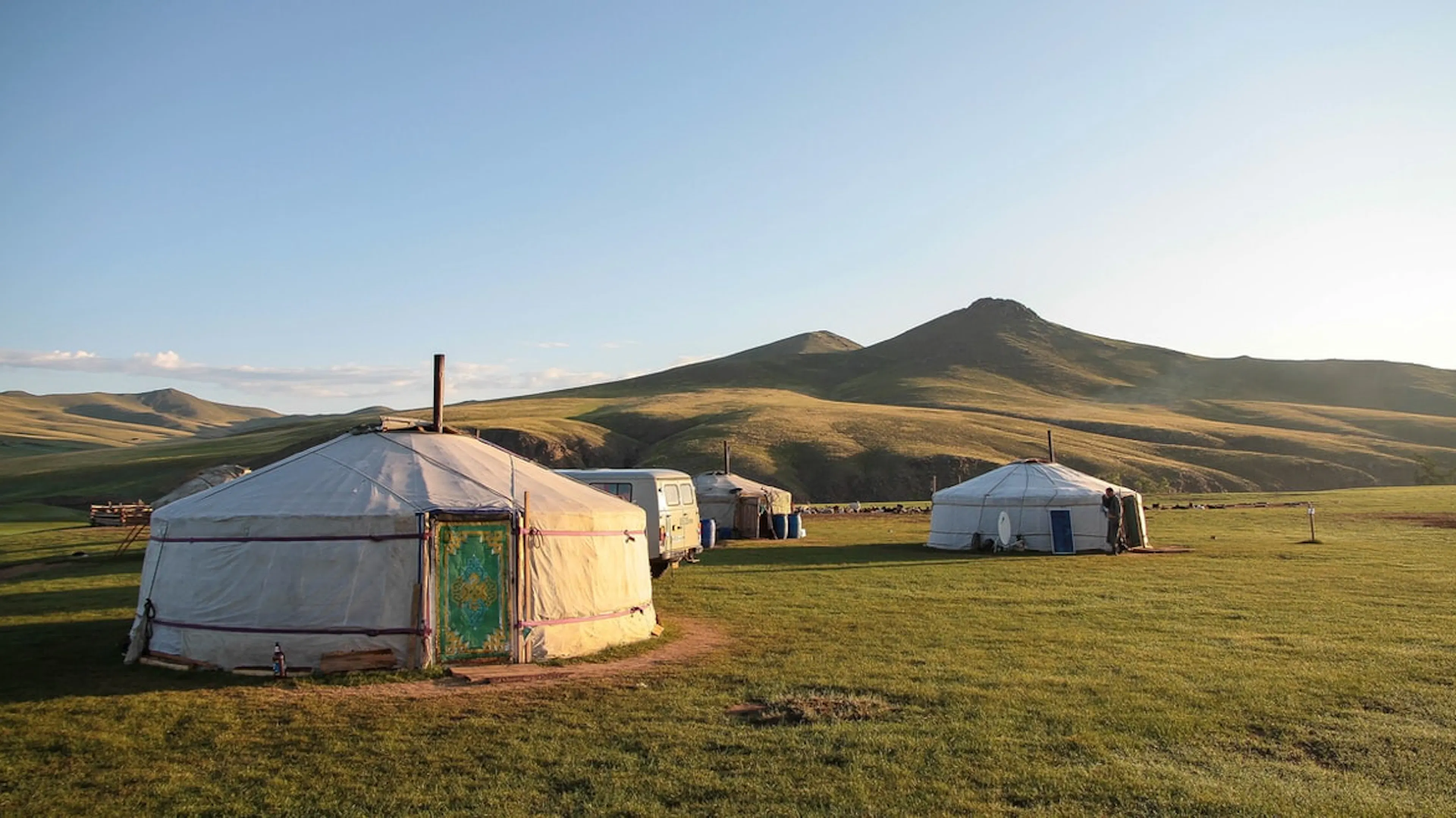 Three white yurts in a green meadow lit by gentle sunrise light under a clear blue sky 