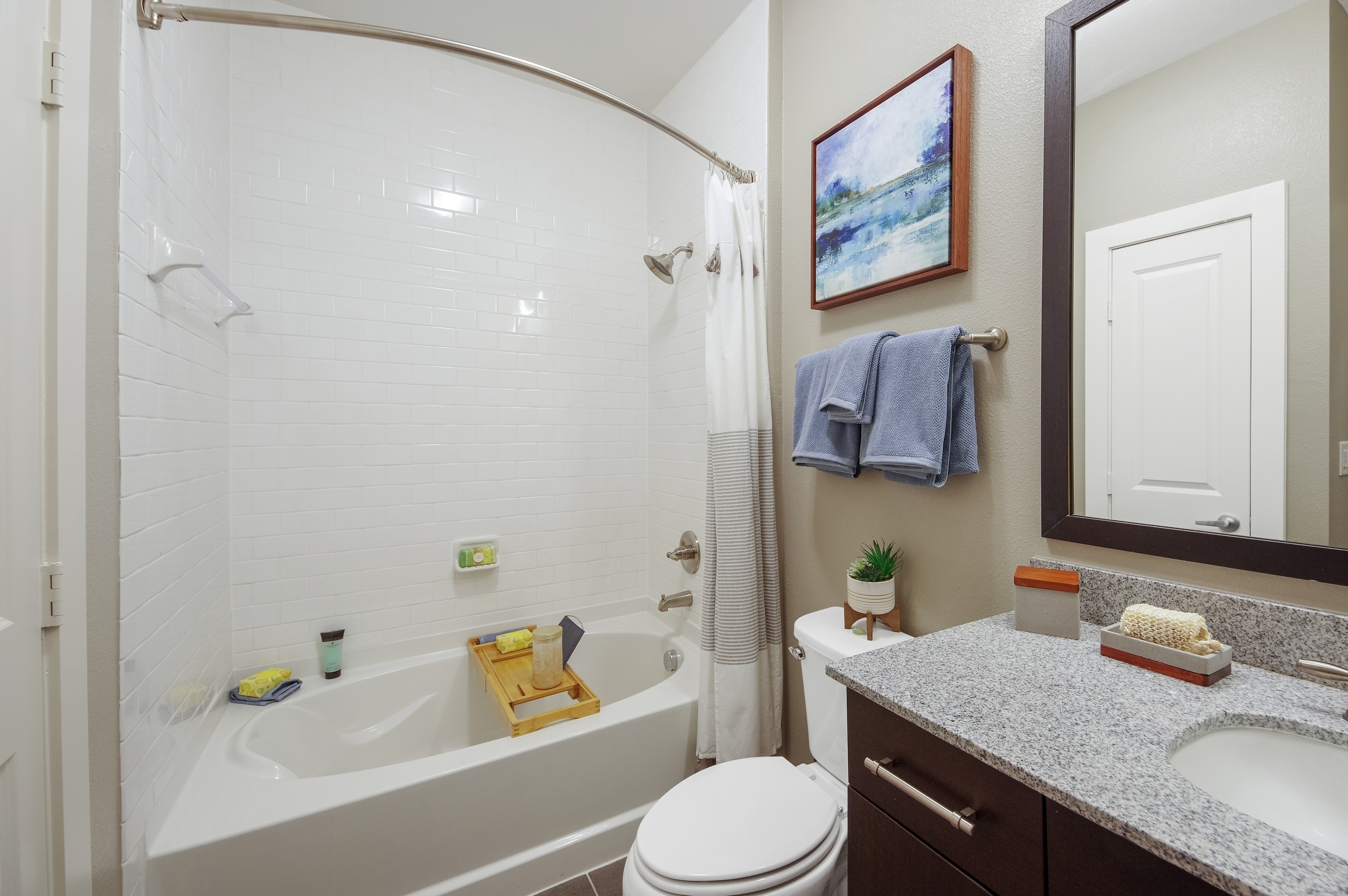 AMLI Riverfront Park apartment bathroom featuring a subway tiled shower tub and a granite dark wood vanity with framed mirror