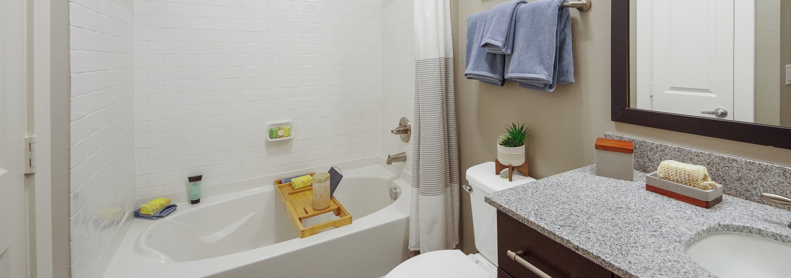 AMLI Riverfront Park apartment bathroom featuring a subway tiled shower tub and a granite dark wood vanity with framed mirror