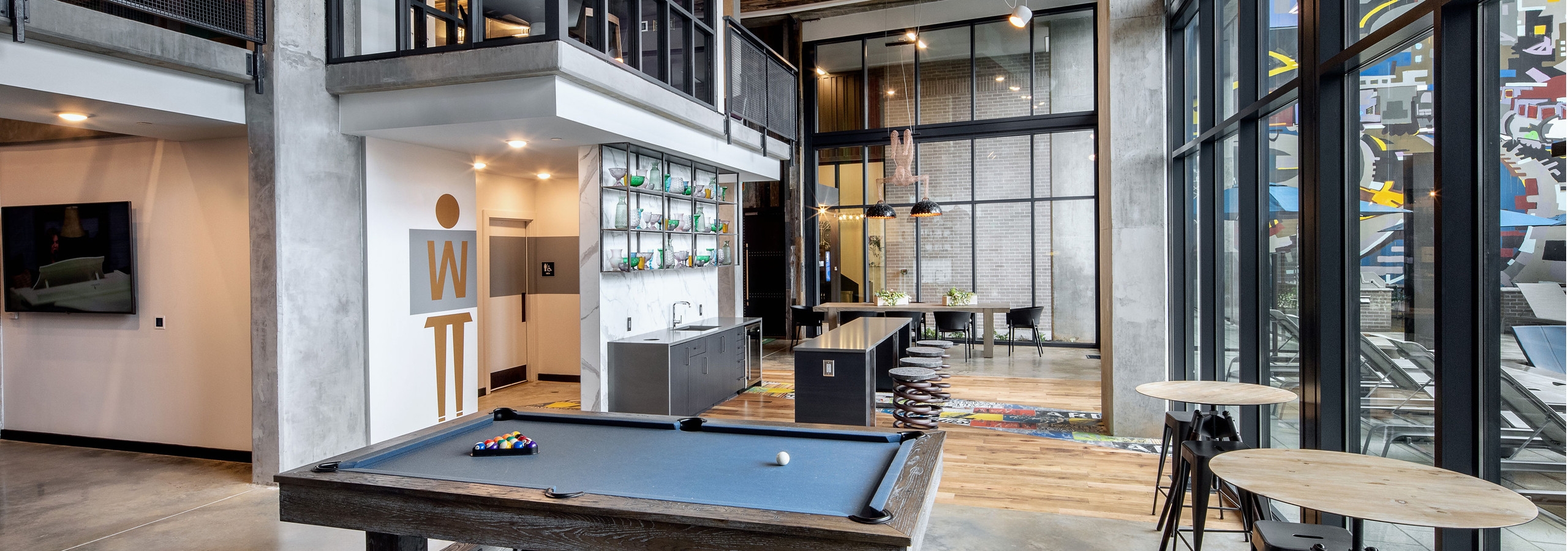 Interior view of AMLI Westside clubroom showing billiards and arcade games with large windows and various seating options