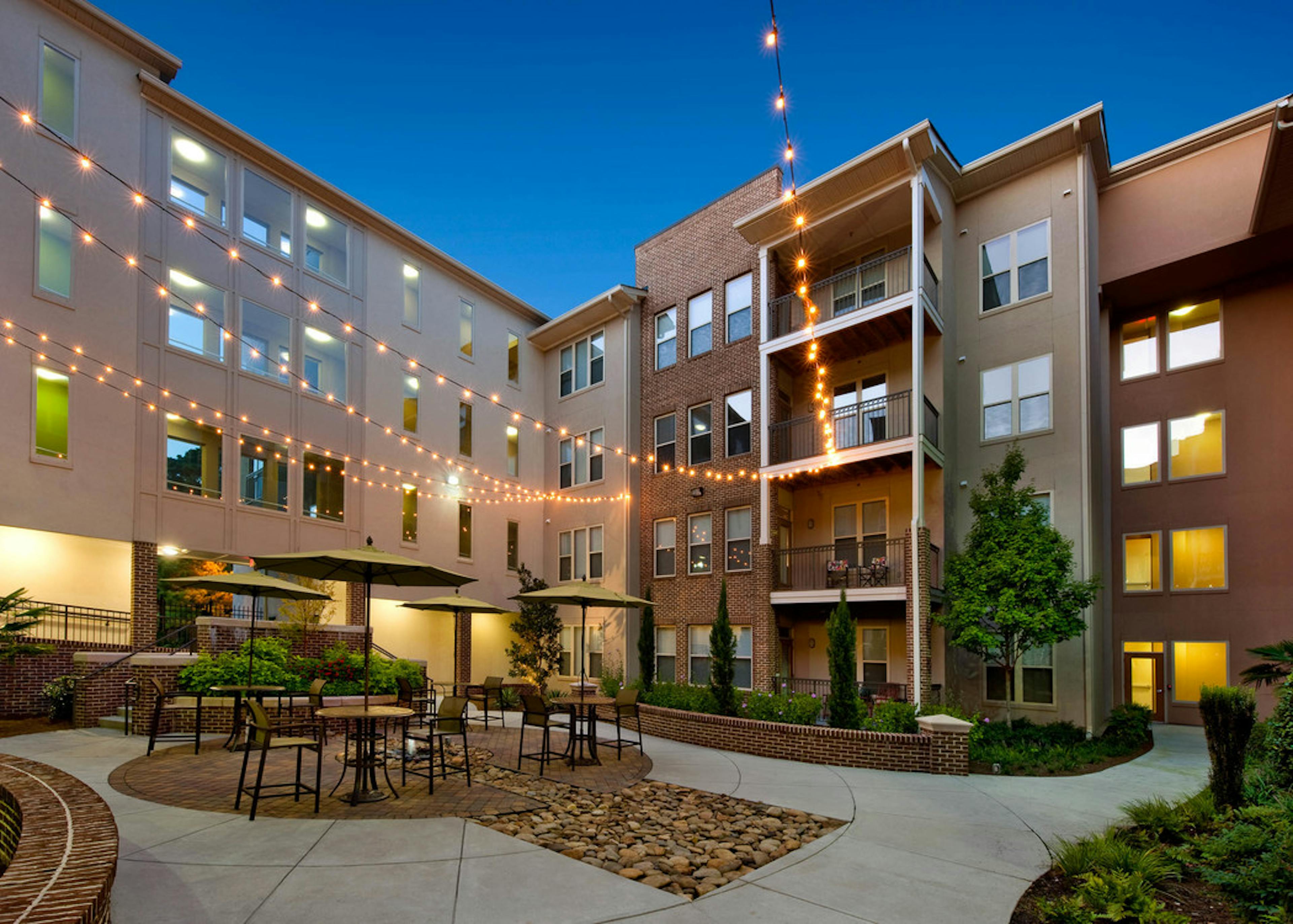 Exterior dusk view of AMLI Lindbergh courtyard on concrete with multiple table and chairs with umbrellas and hanging lights