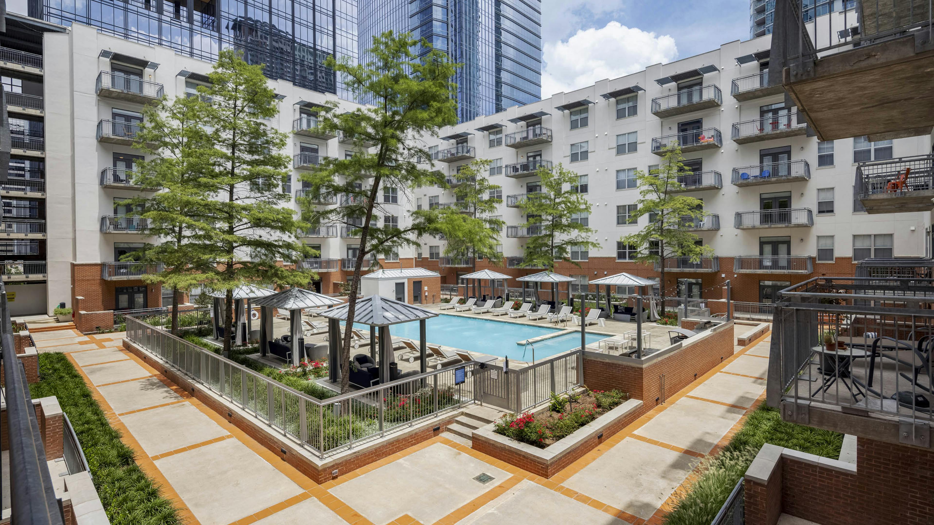 Elevated view of AMLI Downtown courtyard pool with poolside cabanas and a grill station surrounded by tall green trees