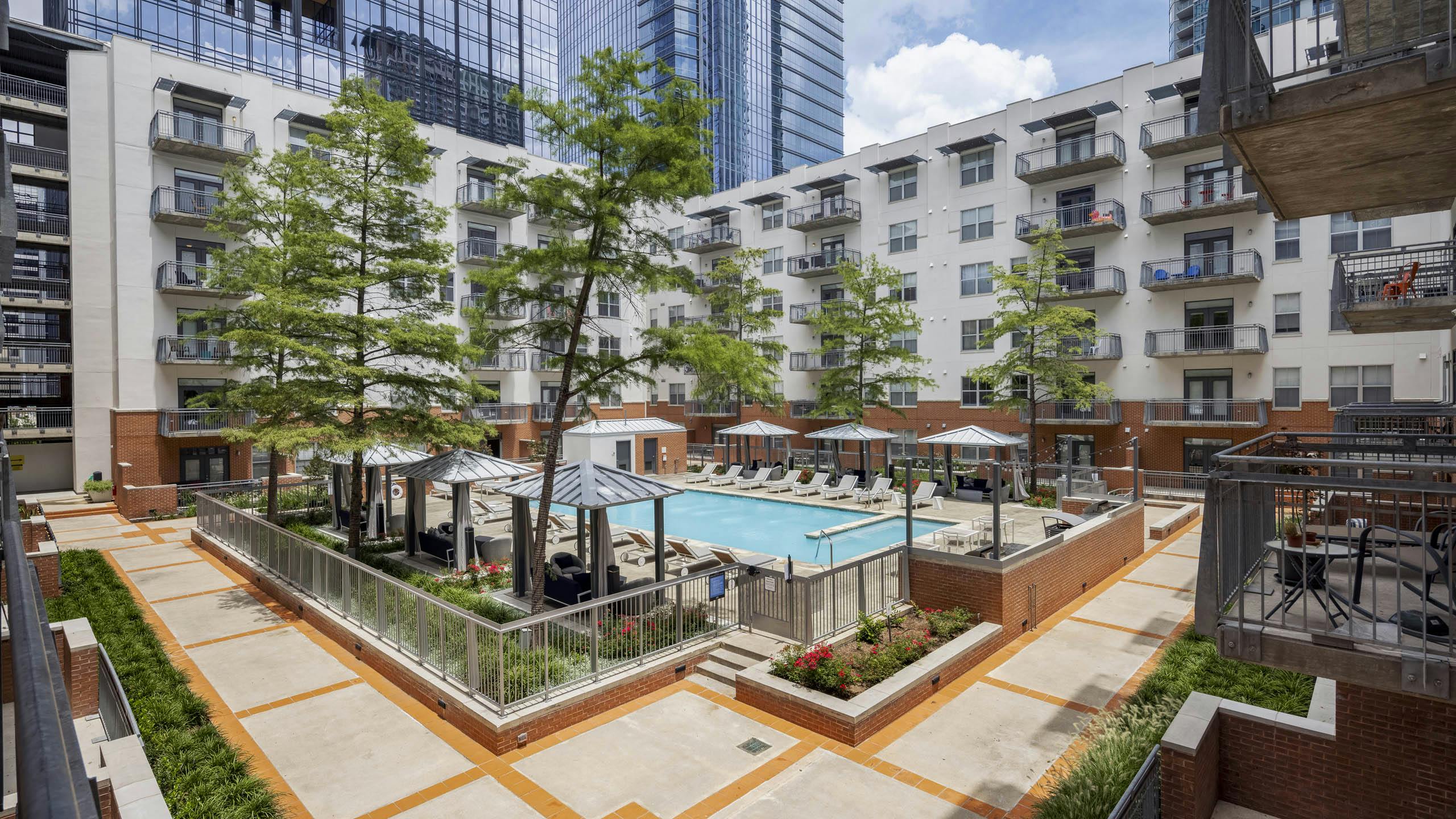 Elevated view of AMLI Downtown courtyard pool with poolside cabanas and a grill station surrounded by tall green trees