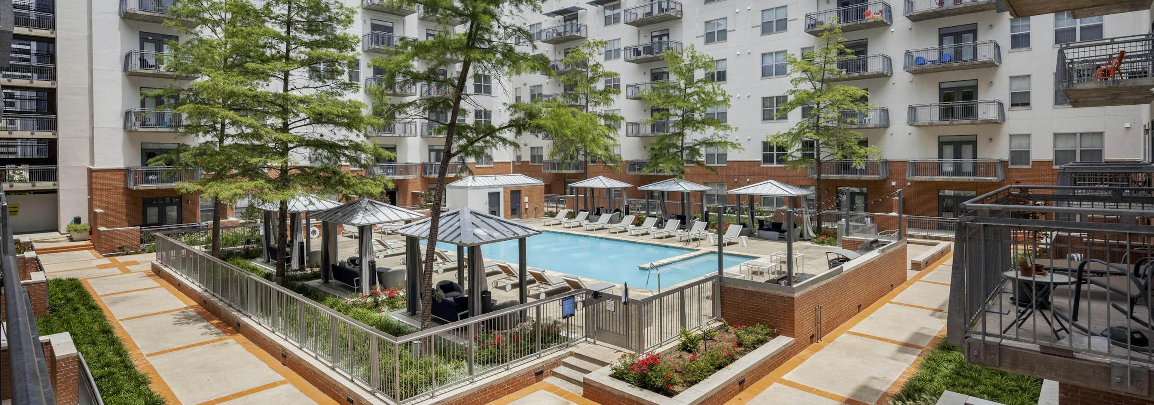 Elevated view of AMLI Downtown courtyard pool with poolside cabanas and a grill station surrounded by tall green trees