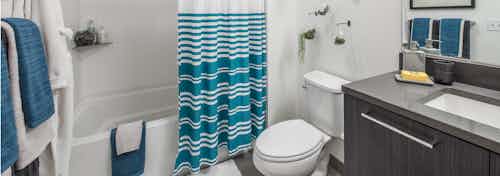Interior view of apartment of AMLI Arc of bathroom dark quartz countertops with toilet and shower and tub combination