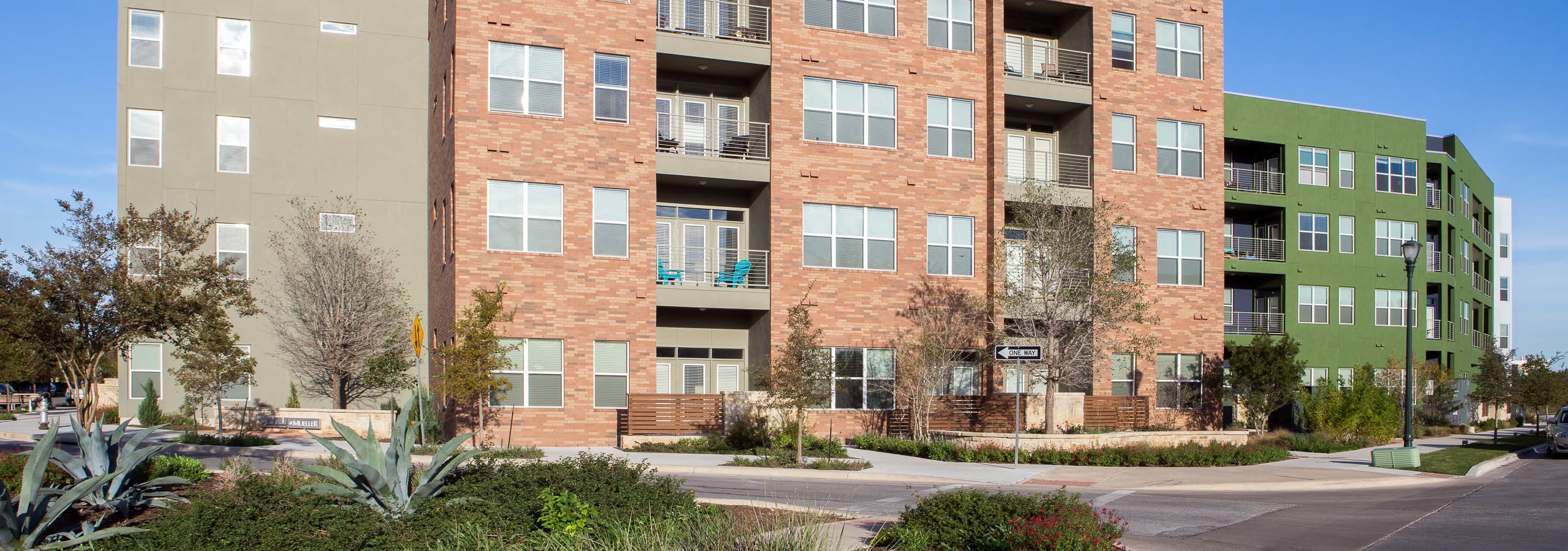 Colorful building exterior of AMLI at Mueller apartment community in front of a vibrant blue sky with surrounding trees