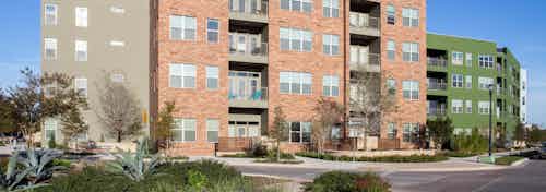 Colorful building exterior of AMLI at Mueller apartment community in front of a vibrant blue sky with surrounding trees