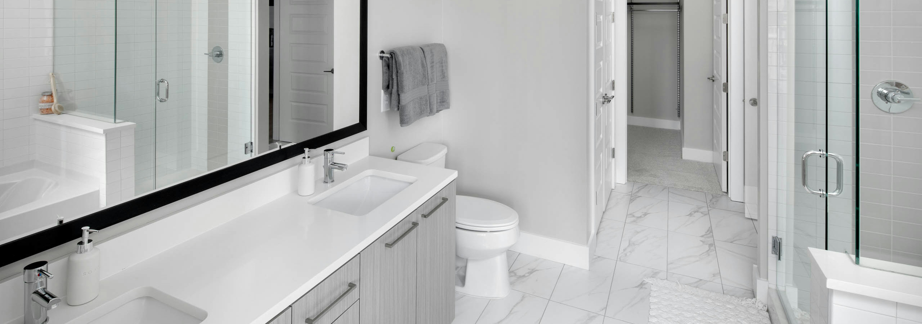 AMLI Arts Center bathroom with a grey double vanity sink and glass door leading into shower with marble patterned floor tile