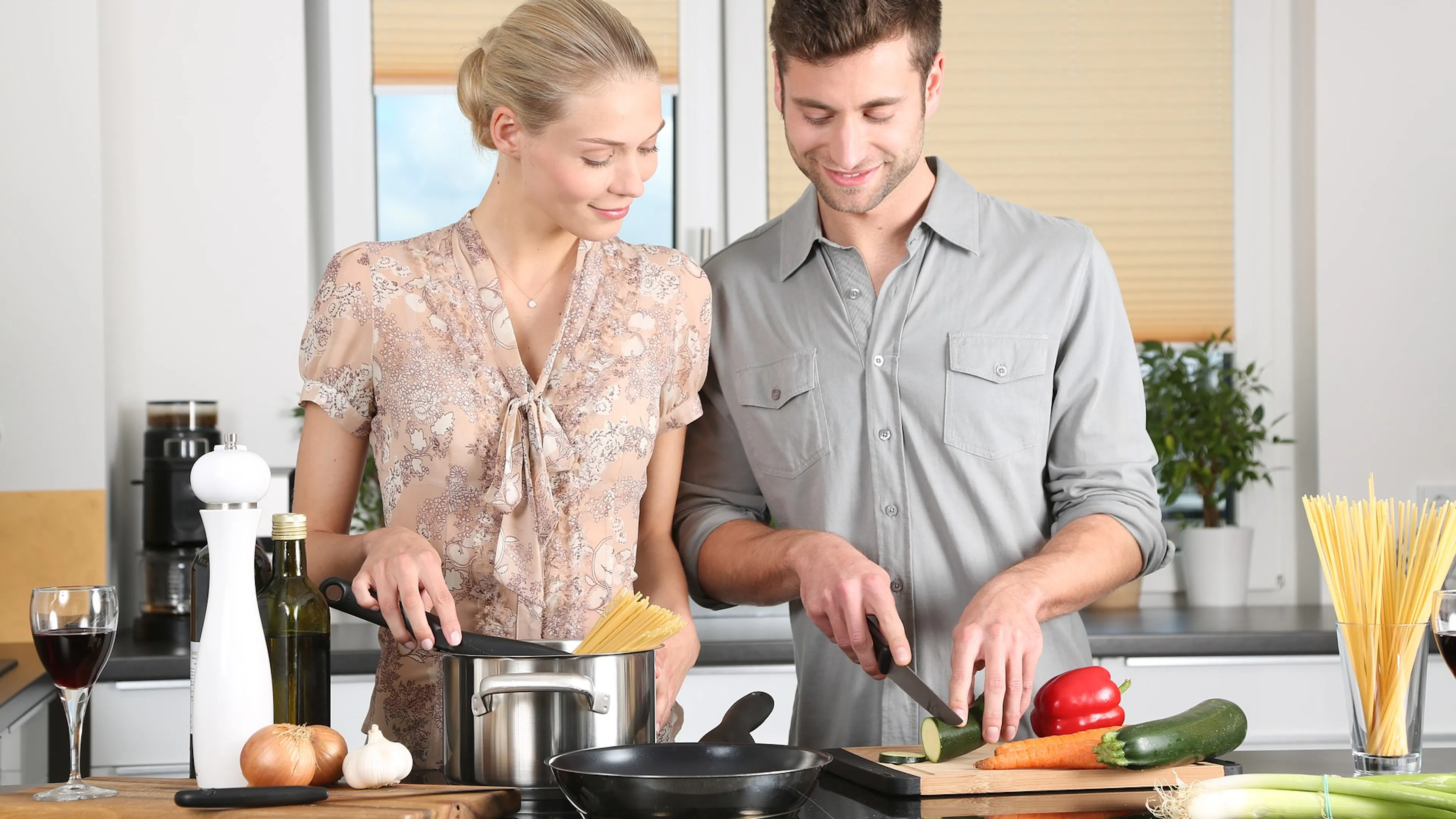A man and a woman side by side cooking pasta and vegetables at a kitchen counter