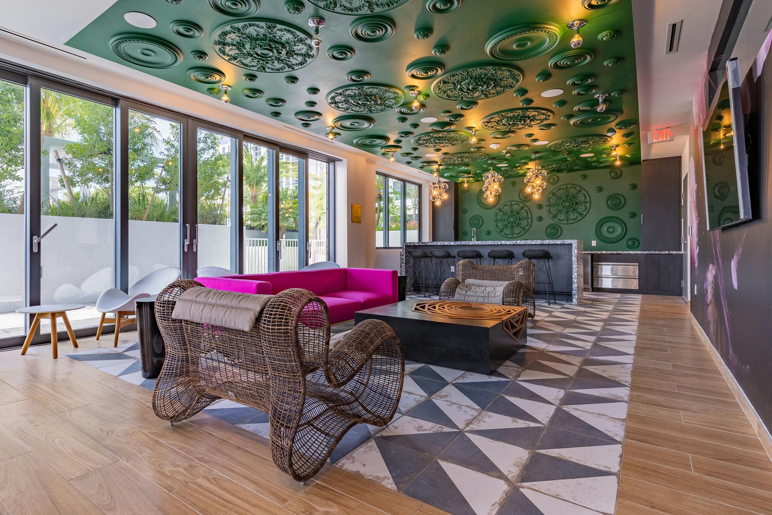 AMLI Midtown Miami resident lounge with oversized woven chairs and pink sofa and black bar against green ornate wall