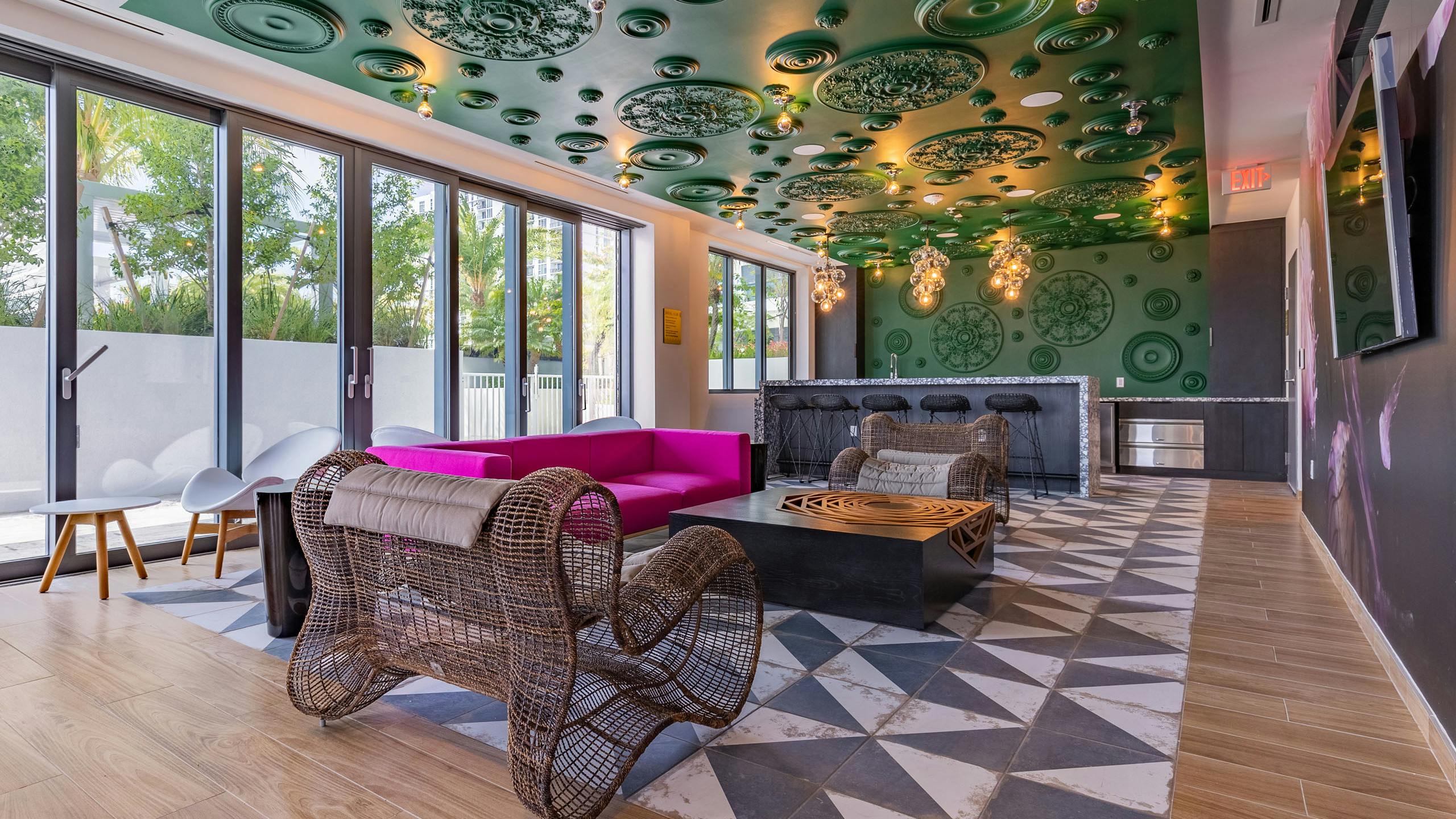 AMLI Midtown Miami resident lounge with oversized woven chairs and pink sofa and black bar against green ornate wall