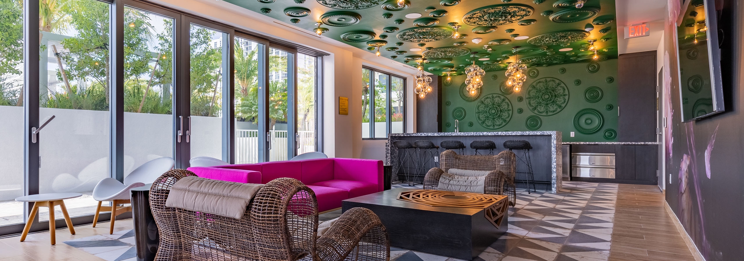 AMLI Midtown Miami resident lounge with oversized woven chairs and pink sofa and black bar against green ornate wall