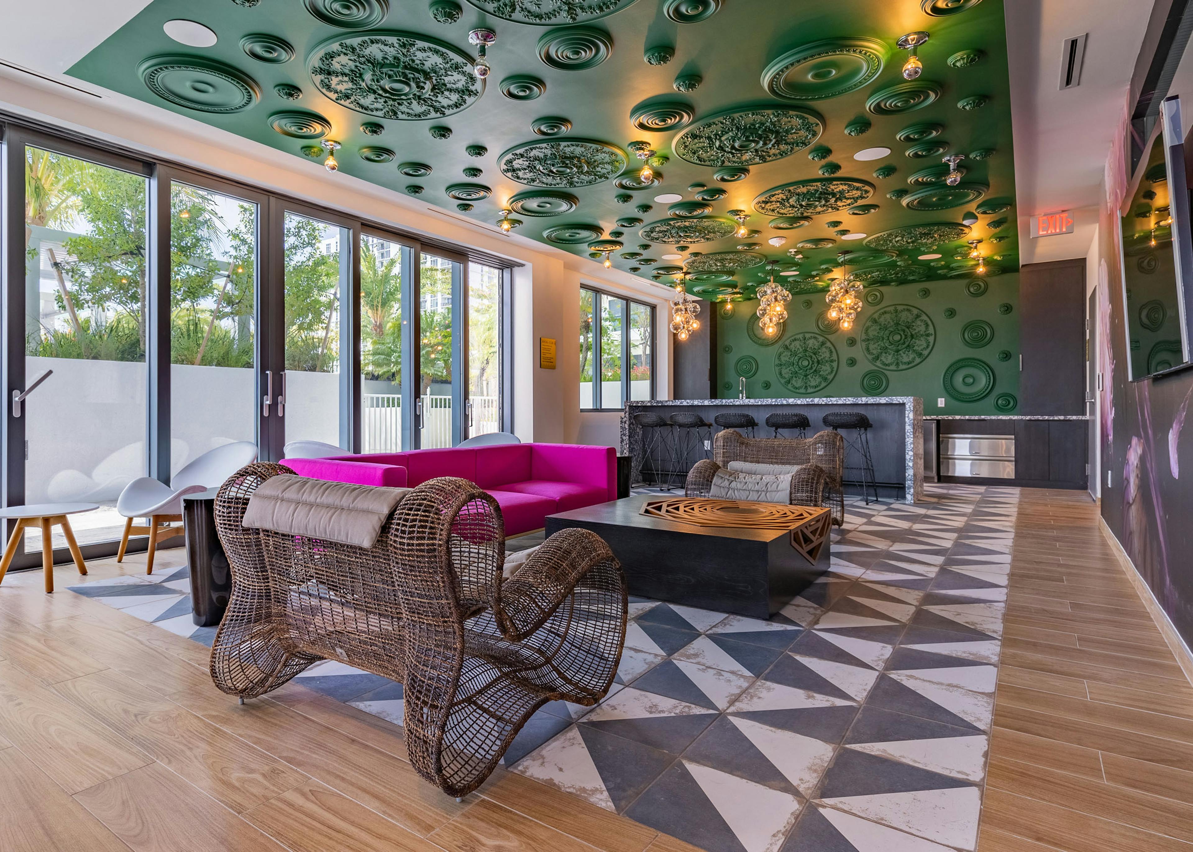 AMLI Midtown Miami resident lounge with oversized woven chairs and pink sofa and black bar against green ornate wall