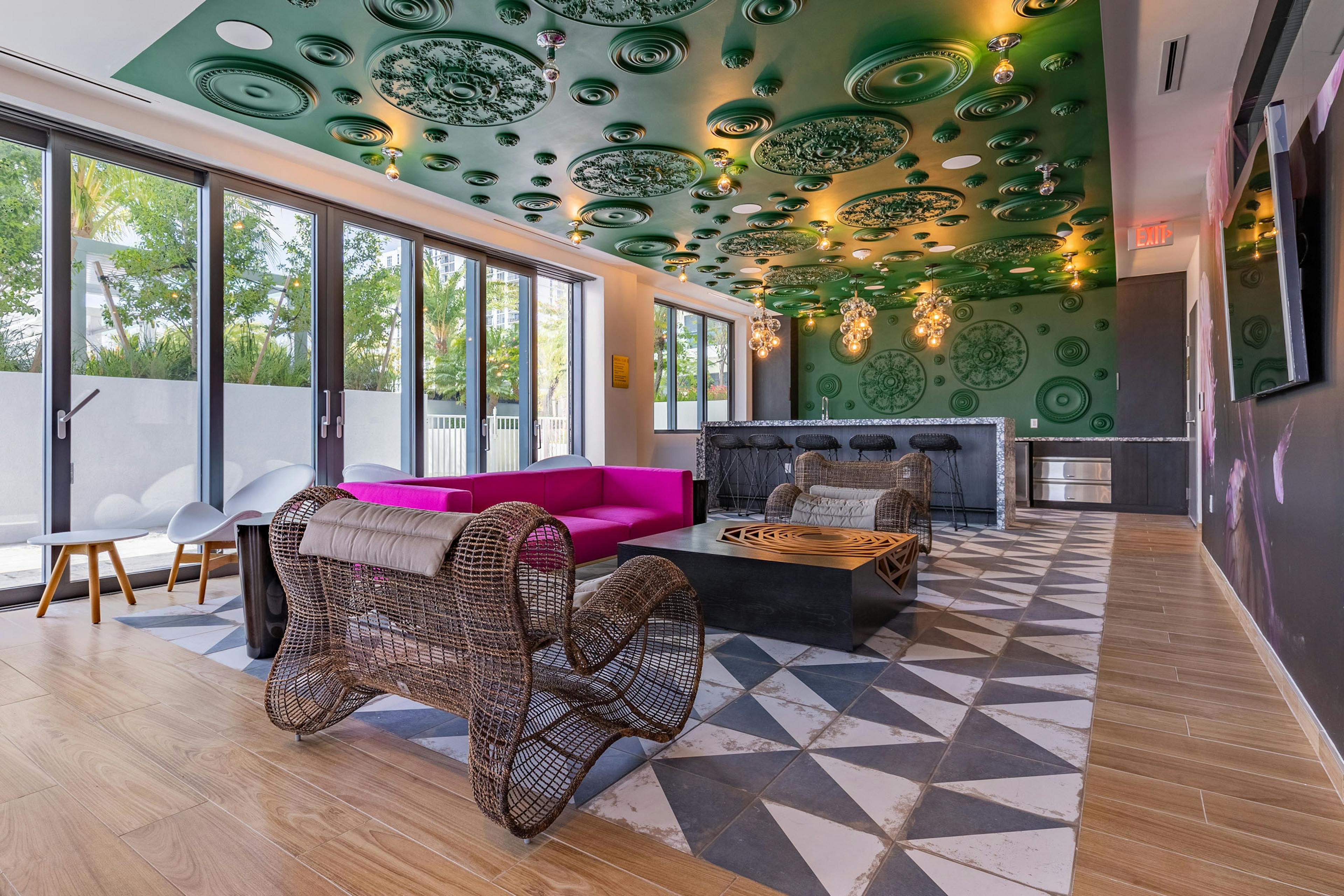 AMLI Midtown Miami resident lounge with oversized woven chairs and pink sofa and black bar against green ornate wall