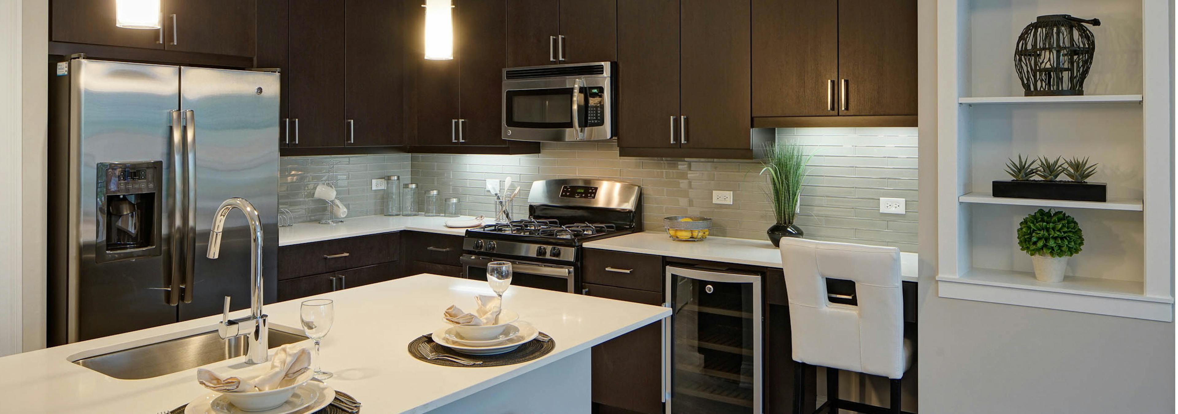 Interior of AMLI Deerfield kitchen with dark wood cabinets and stainless steel appliances with quartz countertop and island  