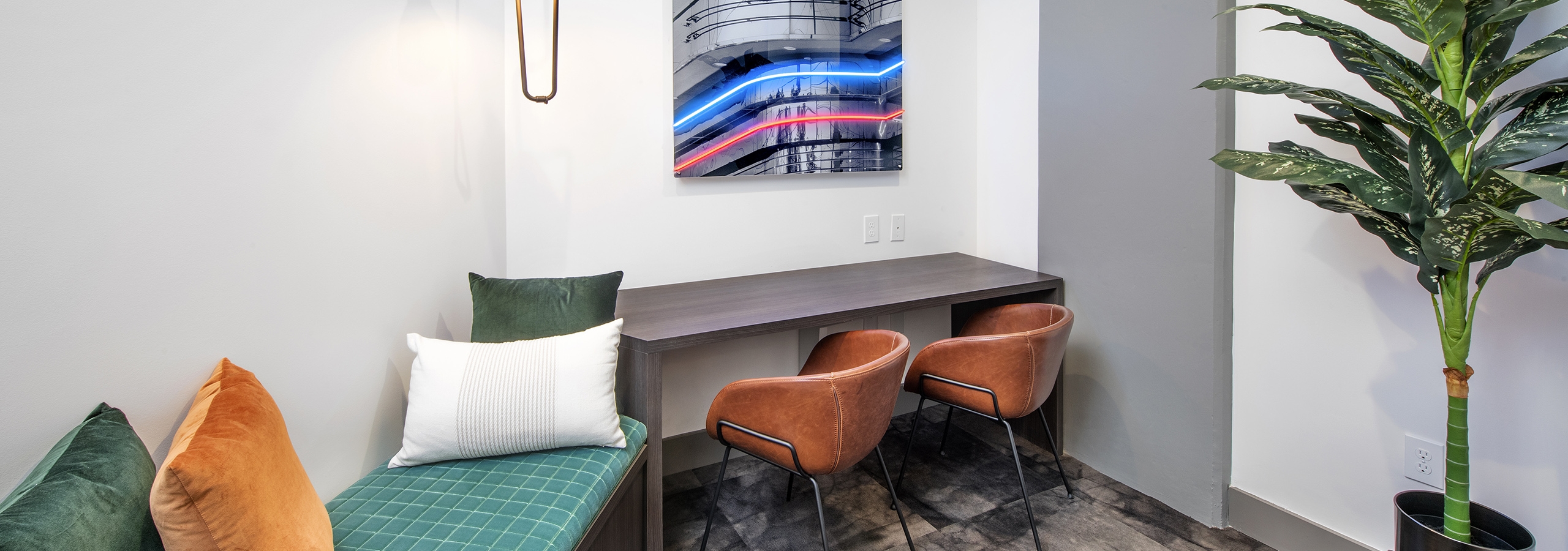 Office at AMLI Flatiron with pendant lighting over green bench and wood desk  with 2 tan leather chairs and neon artwork