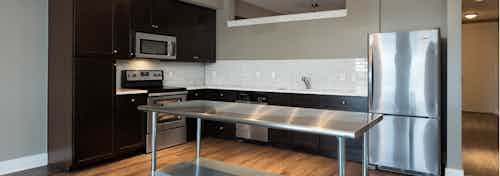 Close up of stainless steel island in AMLI 5350 kitchen with dark cabinets and stainless steel appliances in the background