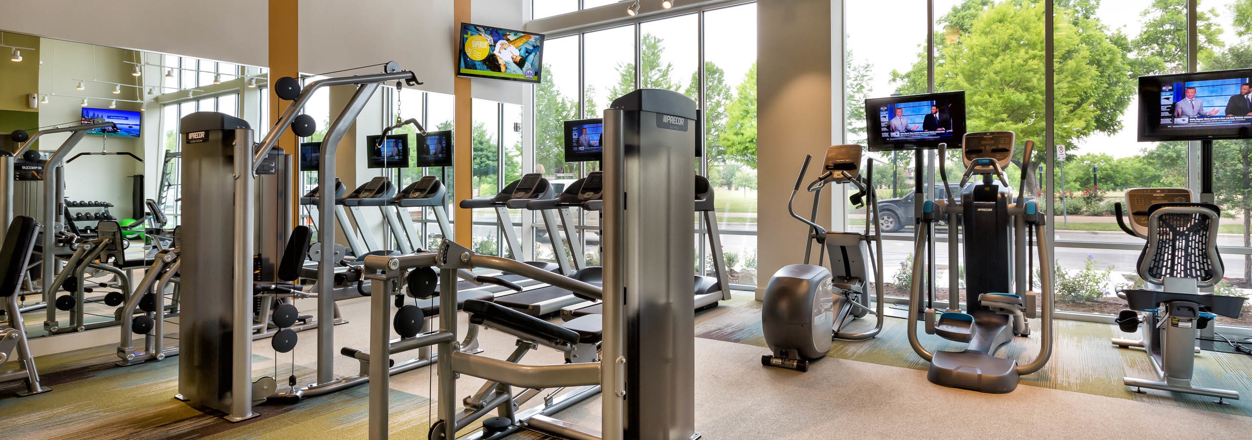 Interior of AMLI at Mueller fitness center with exercise machines facing floor to ceiling windows with daytime scenic view