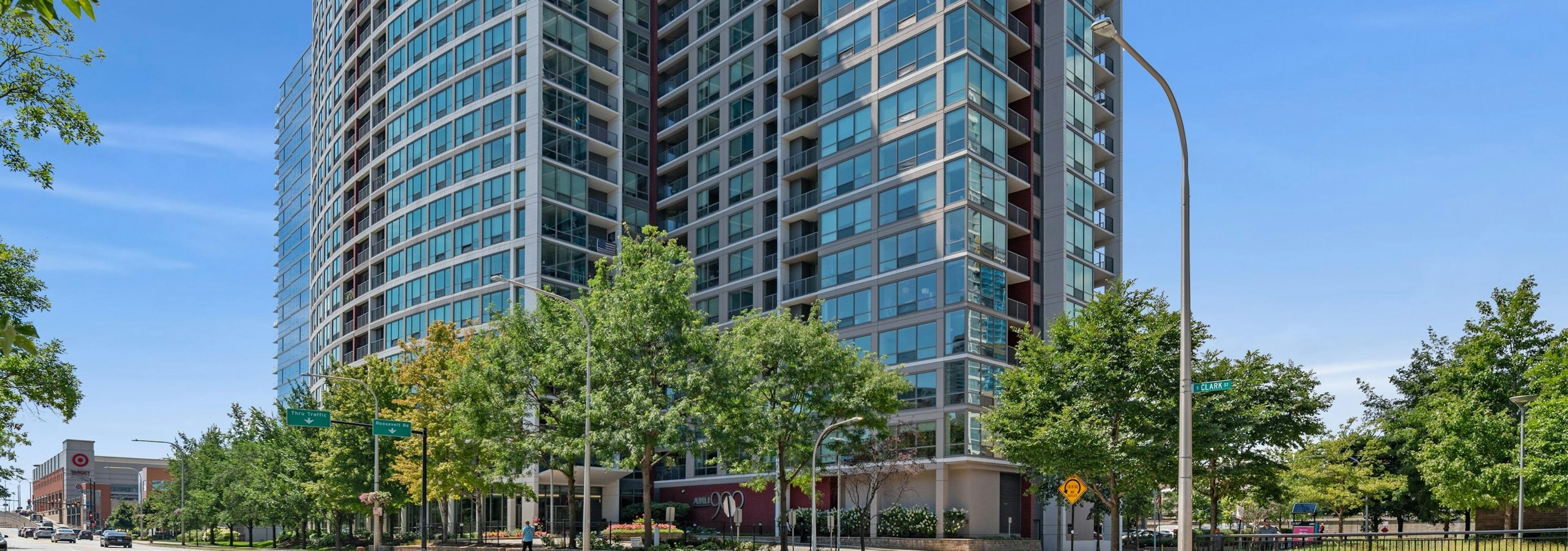 Exterior view of AMLI 900 building with tinted glass windows and concrete balconies overlooking the street lined with trees 