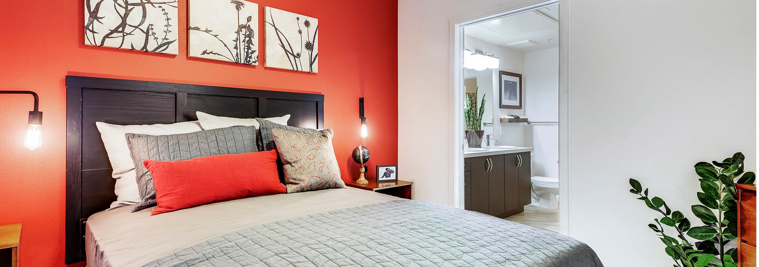 Interior view of a bedroom at AMLI Cherry Creek apartments with a bed backing up to a bright orange wall and view of bathroom