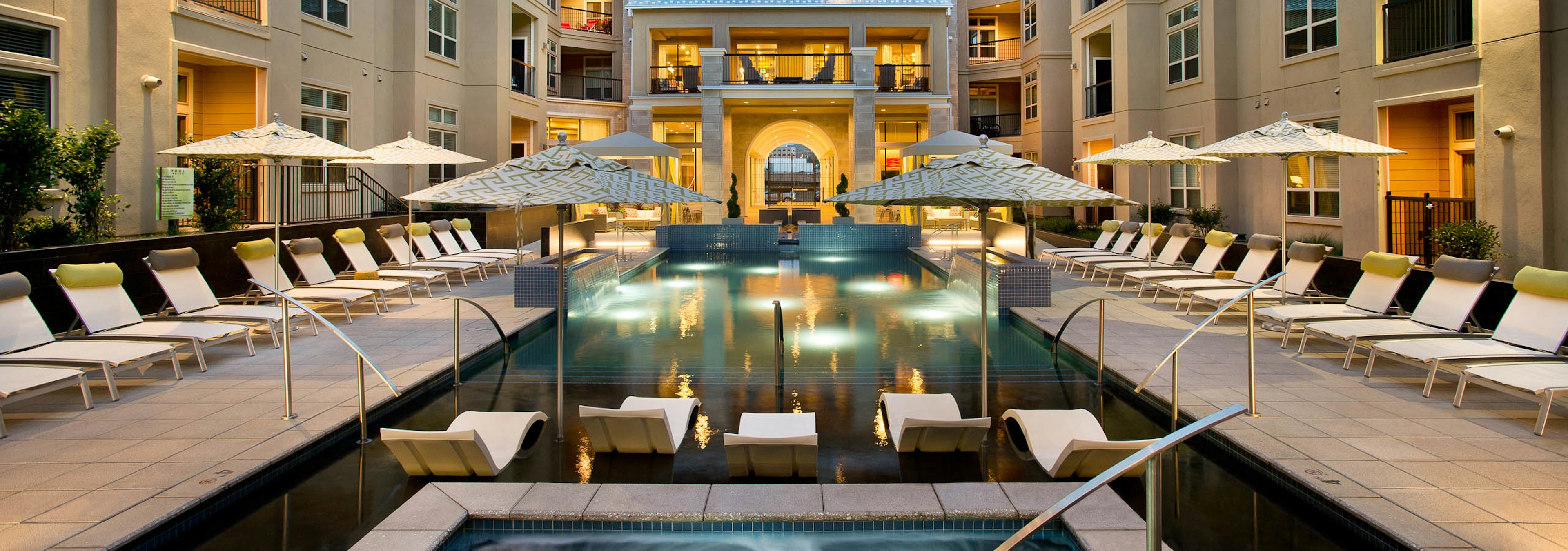 Exterior dusk view of pool close-up with water ledge loungers, steamy Jacuzzi and umbrellas at AMLI RidgeGate apartments