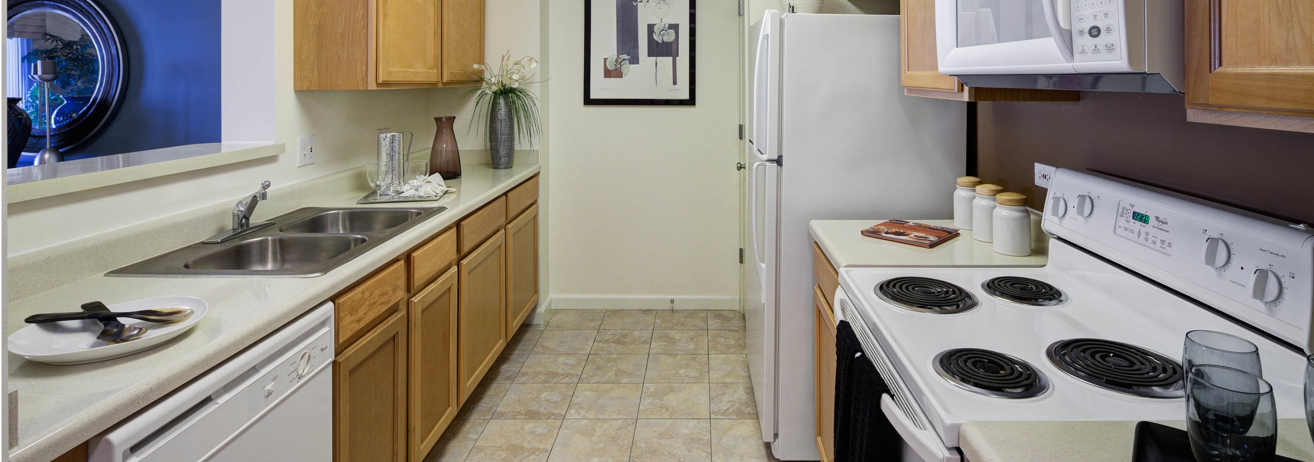 AMLI at Seven Bridges kitchen with medium wood cabinets and white appliances featuring a passthrough window to living area