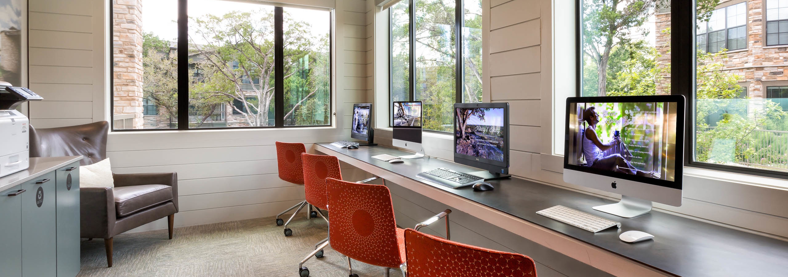 Daytime interior view of AMLI Covered Bridge’s well-lit resident business center with four desktop monitors