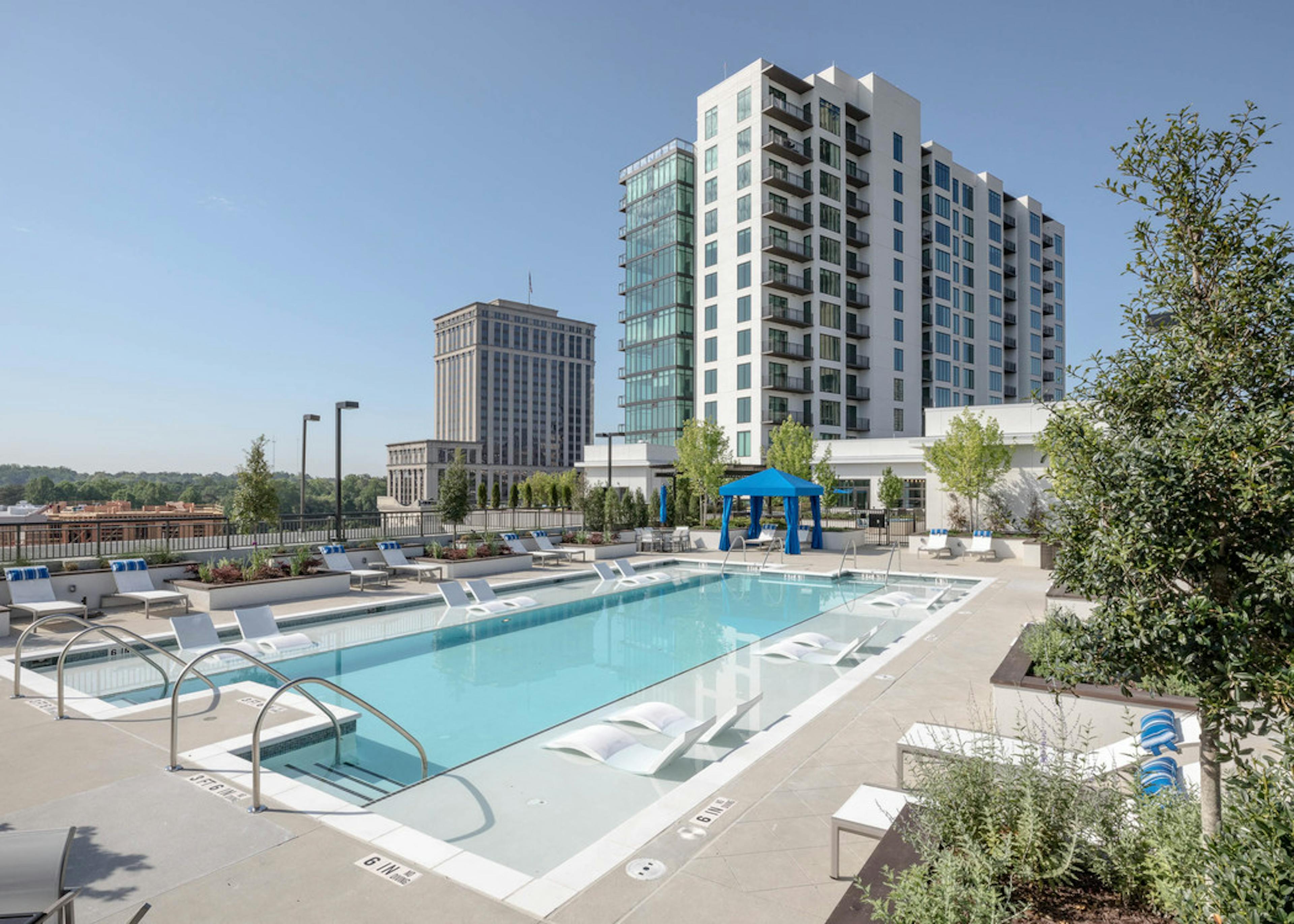 Daytime view of the pool at AMLI 3464 with surrounding white lounge chairs and a royal blue canopy in the background 