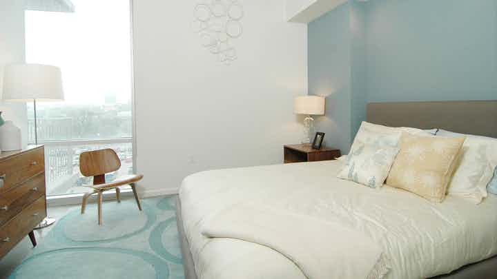AMLI on 2ND bedroom with a blue geometric carpet and floor to ceiling window panel and light blue accent wall behind a large white bed