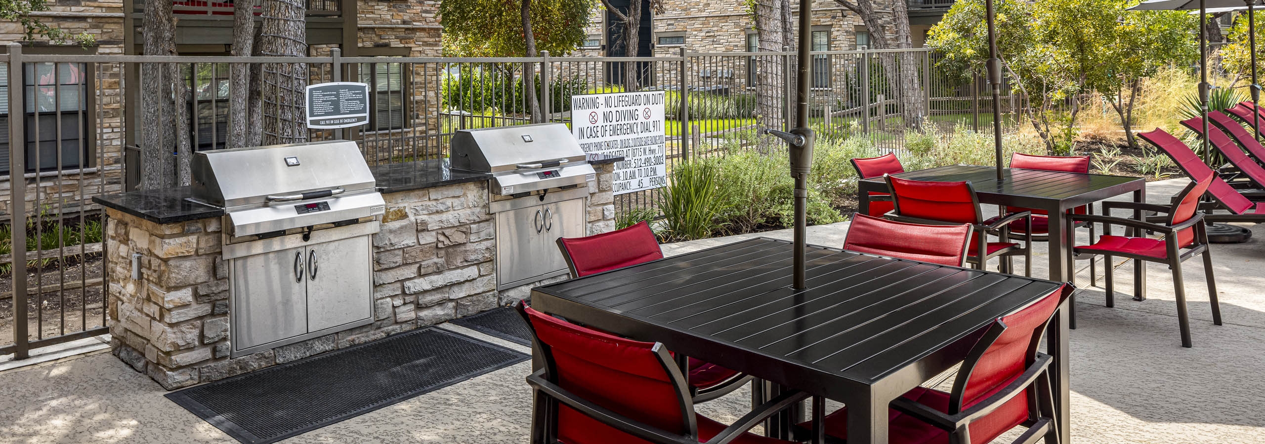 View of grill station with two large outdoor grills and black tables with red chairs and umbrellas at AMLI Covered Bridge