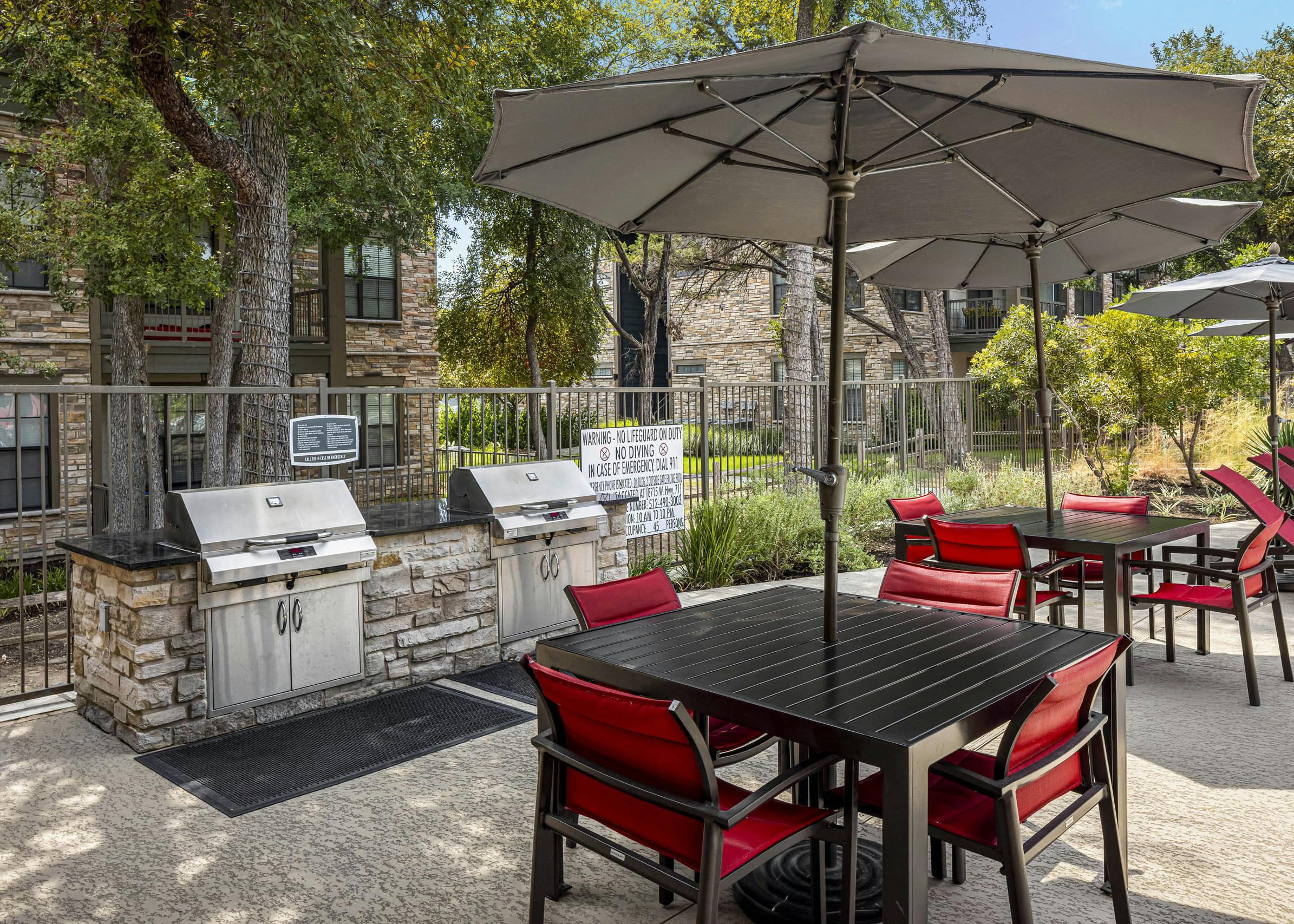 View of grill station with two large outdoor grills and black tables with red chairs and umbrellas at AMLI Covered Bridge