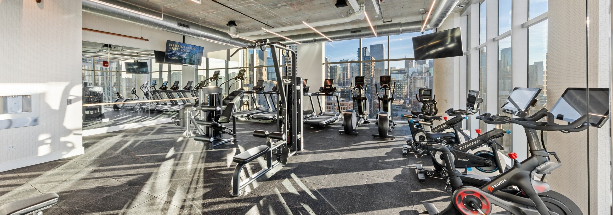 AMLI 808 fitness center surrounded by large windows with loft ceilings and exercise machines facing Chicago skyline view