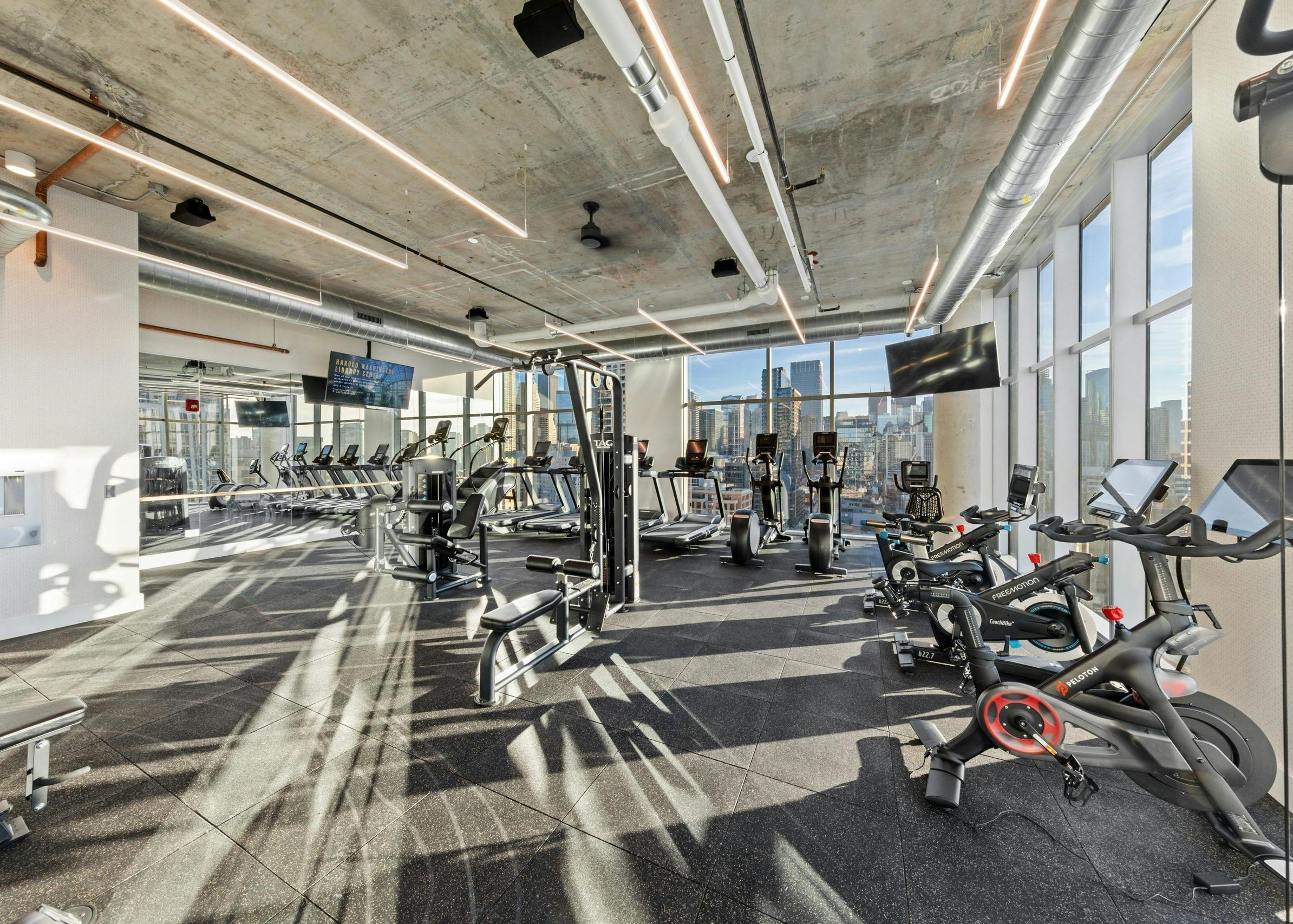 AMLI 808 fitness center surrounded by large windows with loft ceilings and exercise machines facing Chicago skyline view