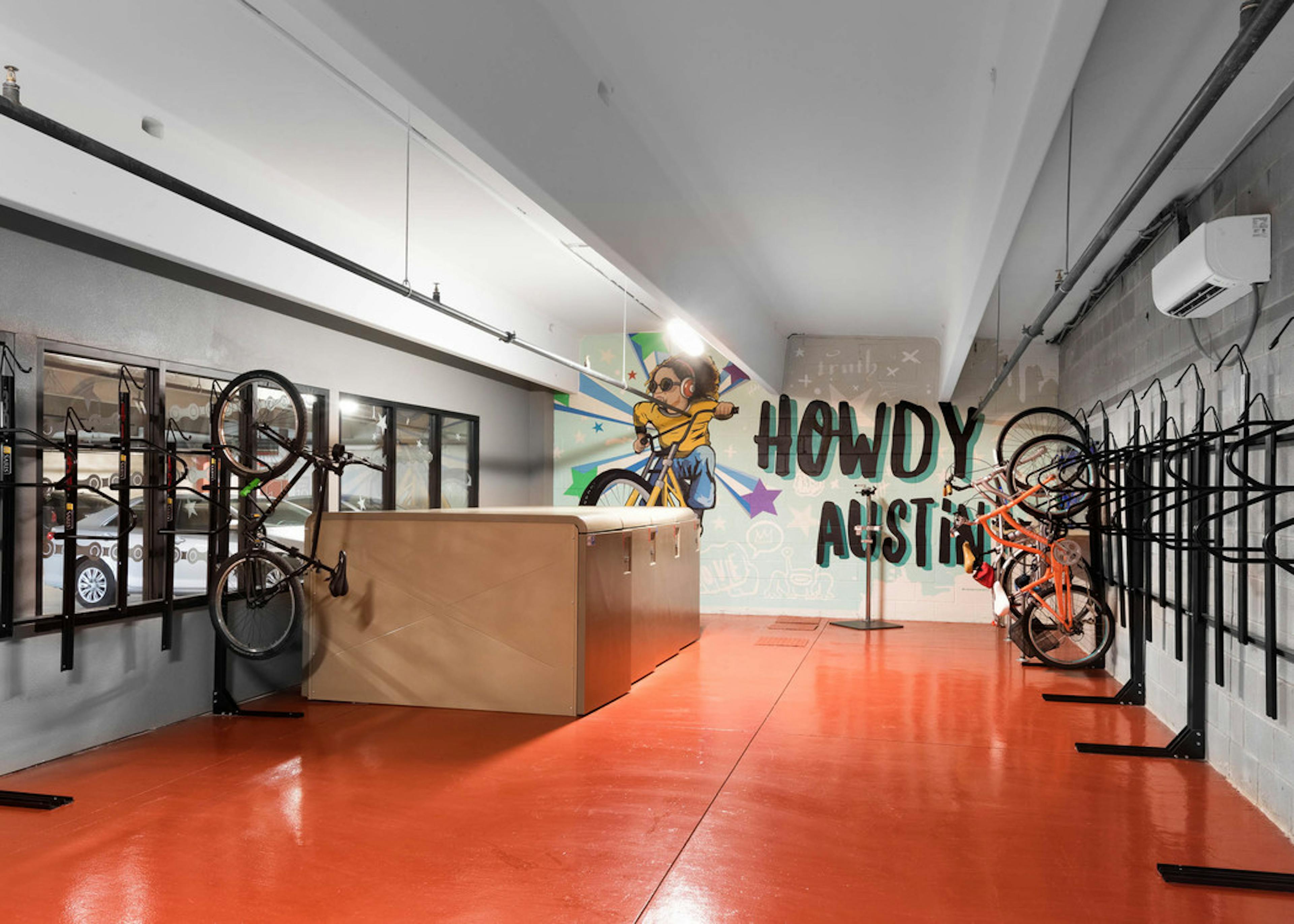 AMLI on Aldrich bike storage room with bikes hanging vertically in black racks and a bright wall stencil reading Howdy Austin