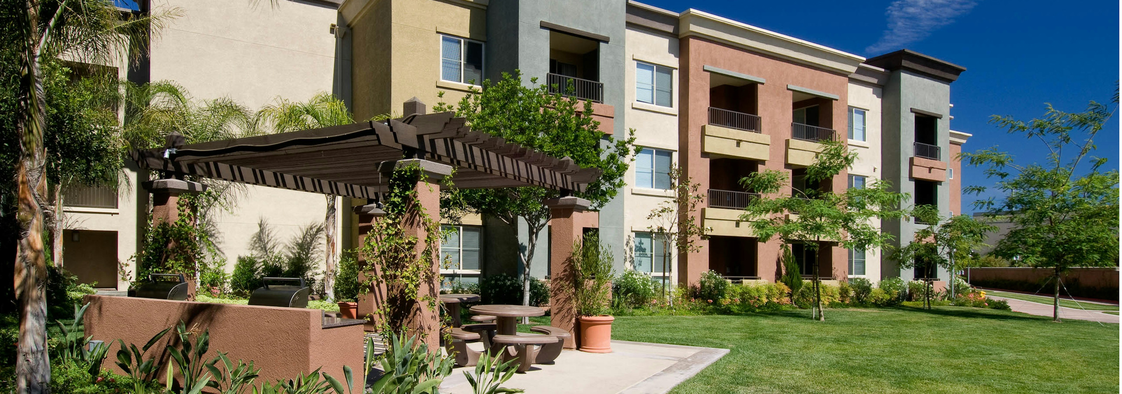 Exterior daytime view of AMLI Warner Center apartment trellis with greenery, grill station picnic area in open grass area