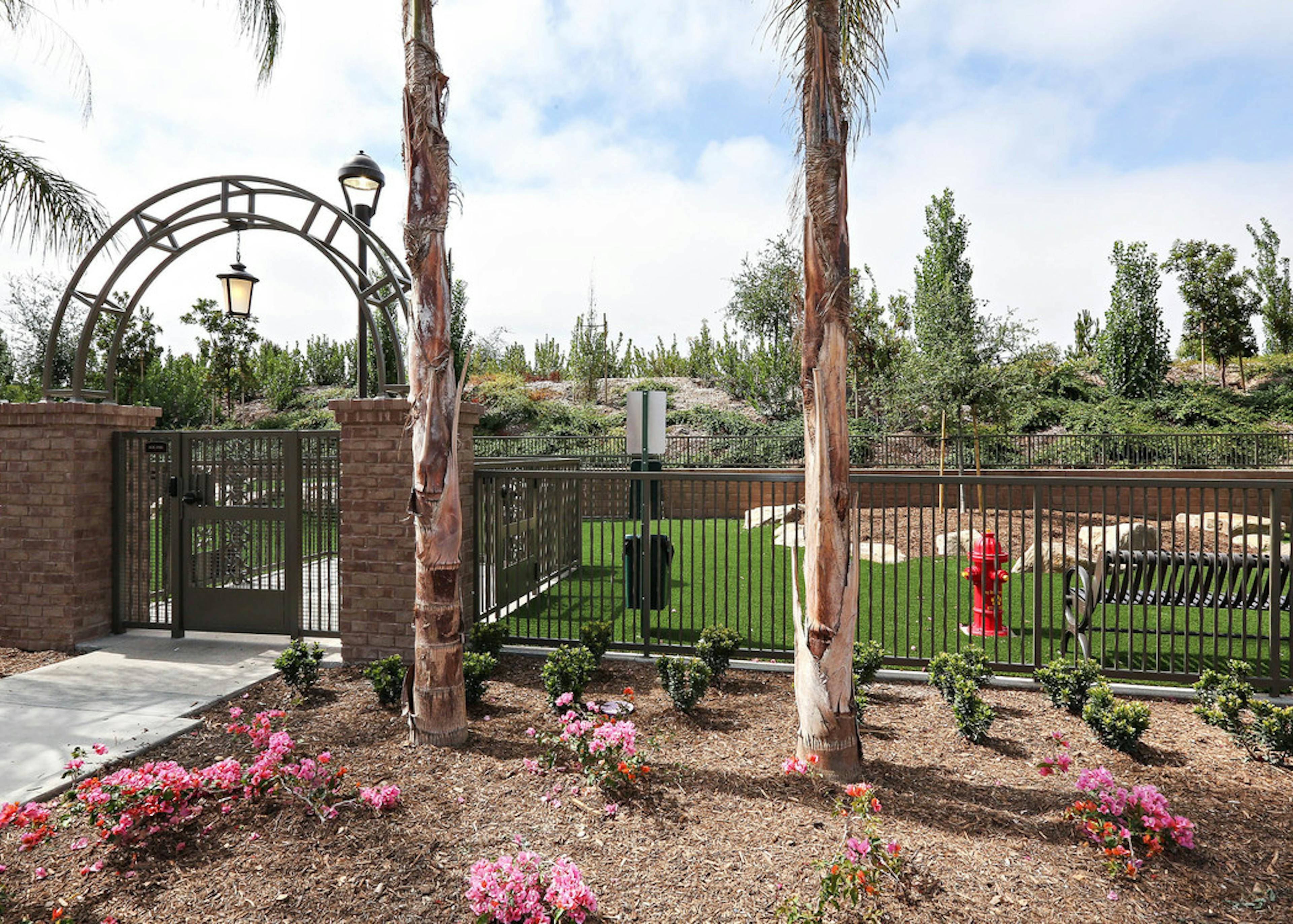 Daytime view of Dog Park’s arched entrance with fence, turf and pet waste station at AMLI Spanish Hills apartment building