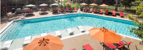 Daytime view of AMLI Covered Bridge pool with orange umbrellas, red lounge chairs, and lush surrounding greenery