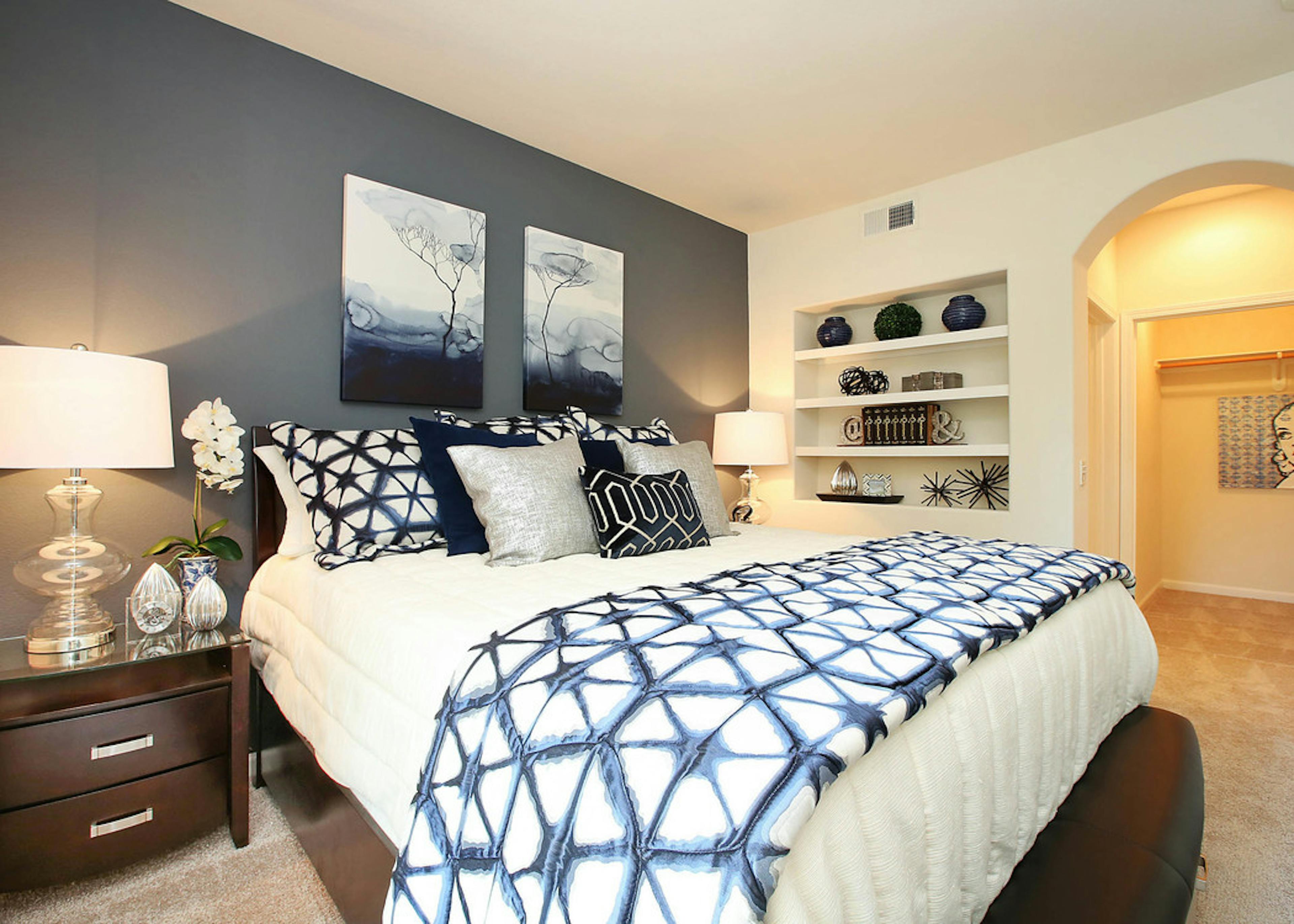 Interior of AMLI Warner Center apartment bedroom with king size bed with decorative pillows, built-in bookshelf and closet